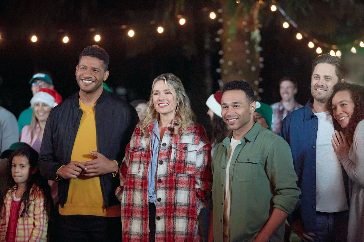 Group of people standing under string of lights in the Hallmark Channel movie 'Campfire Christmas'