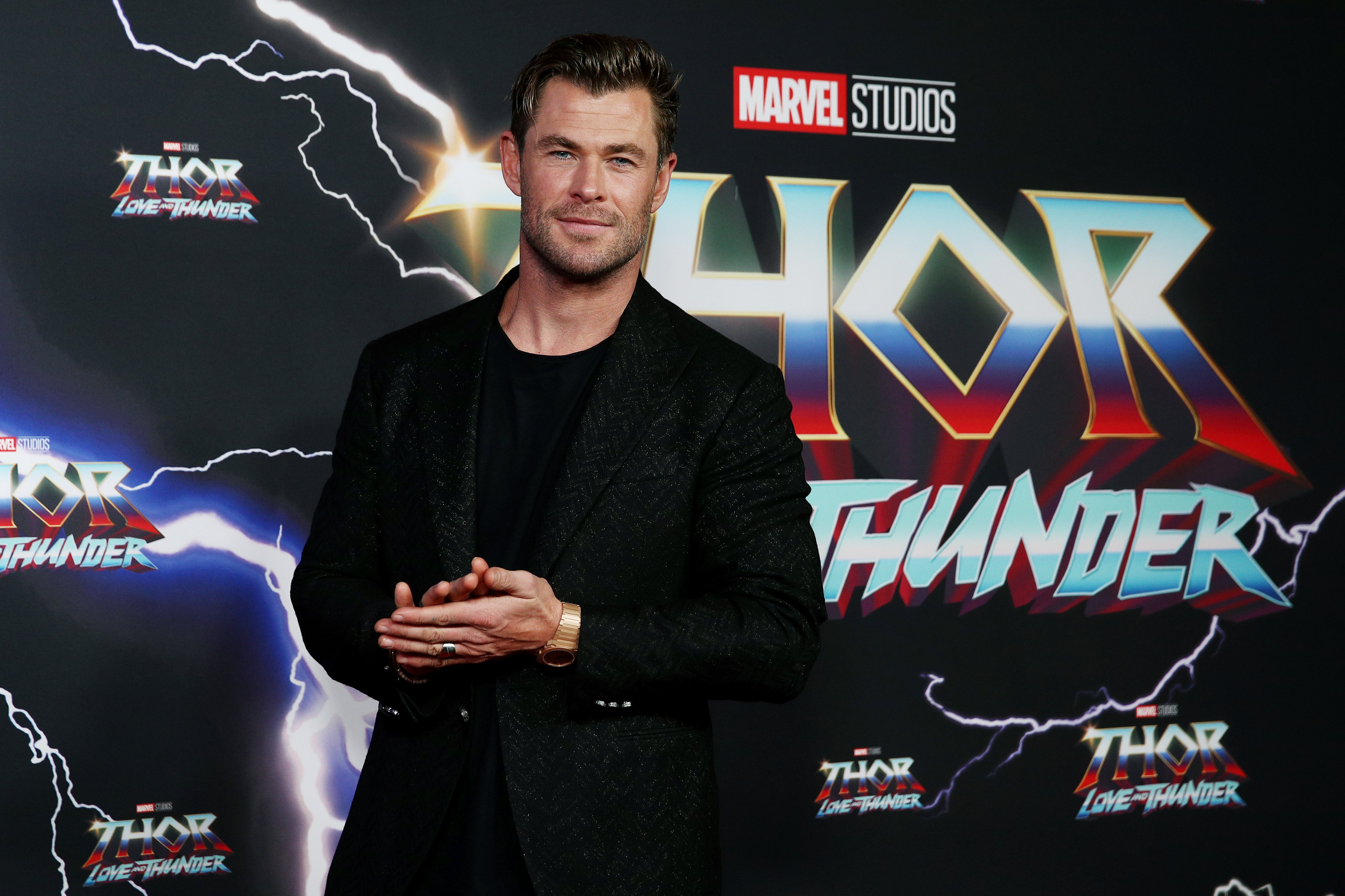 Chris Hemsworth, who stars as Thor in the MCU, wears a black suit over a black shirt.