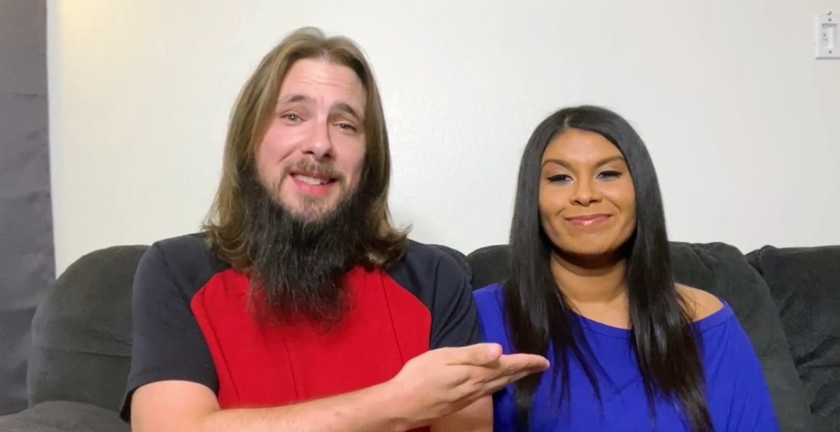 Colt Johnson wears a red shirt and gestures to his wife, Vanessa Guerra, sitting by him on the couch on '90 Day Diaries' on discovery+.