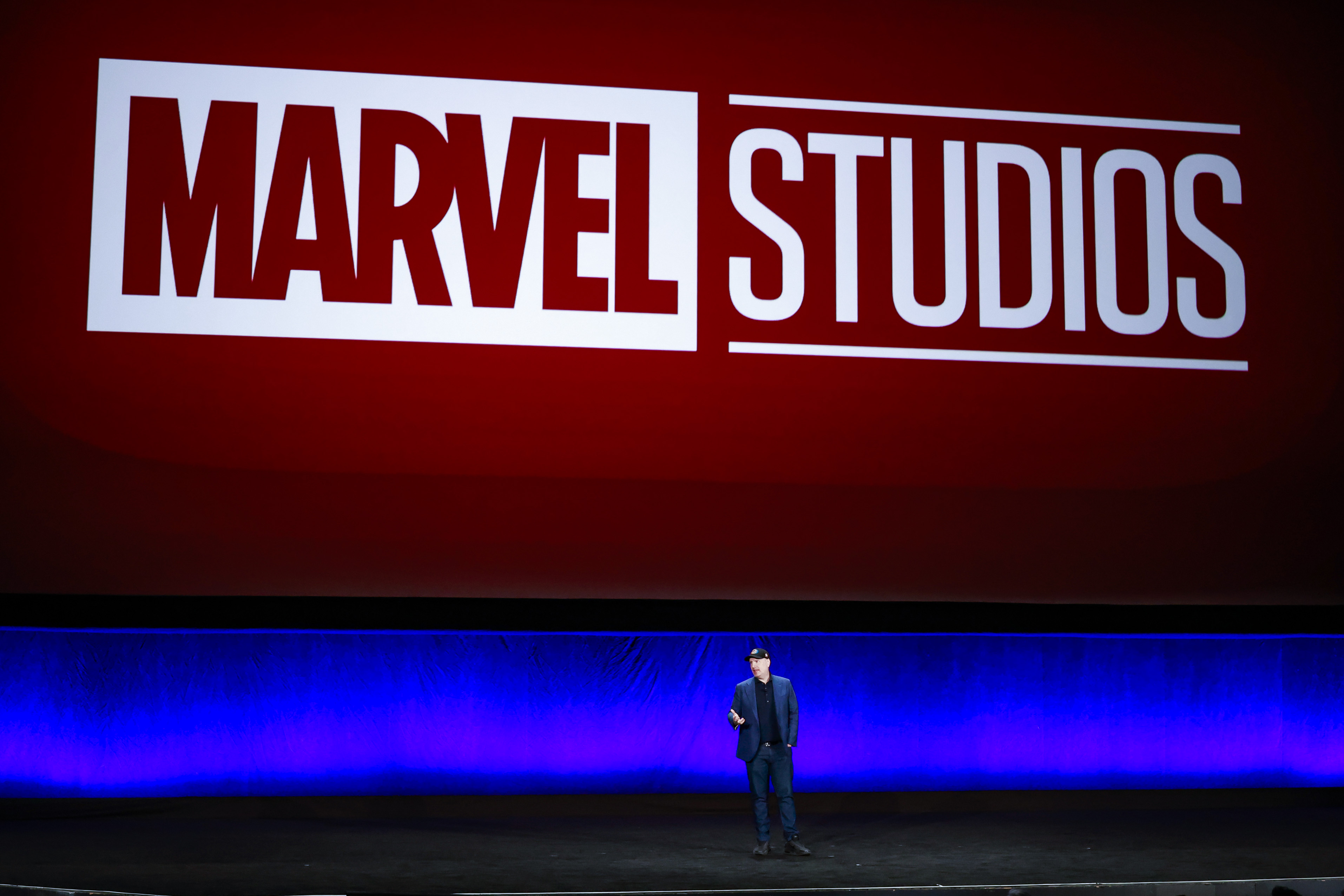 Kevin Feige, who will appear at the Marvel panel during San Diego Comic-Con 2022, stands onstage in front of a sign for Marvel Studios.