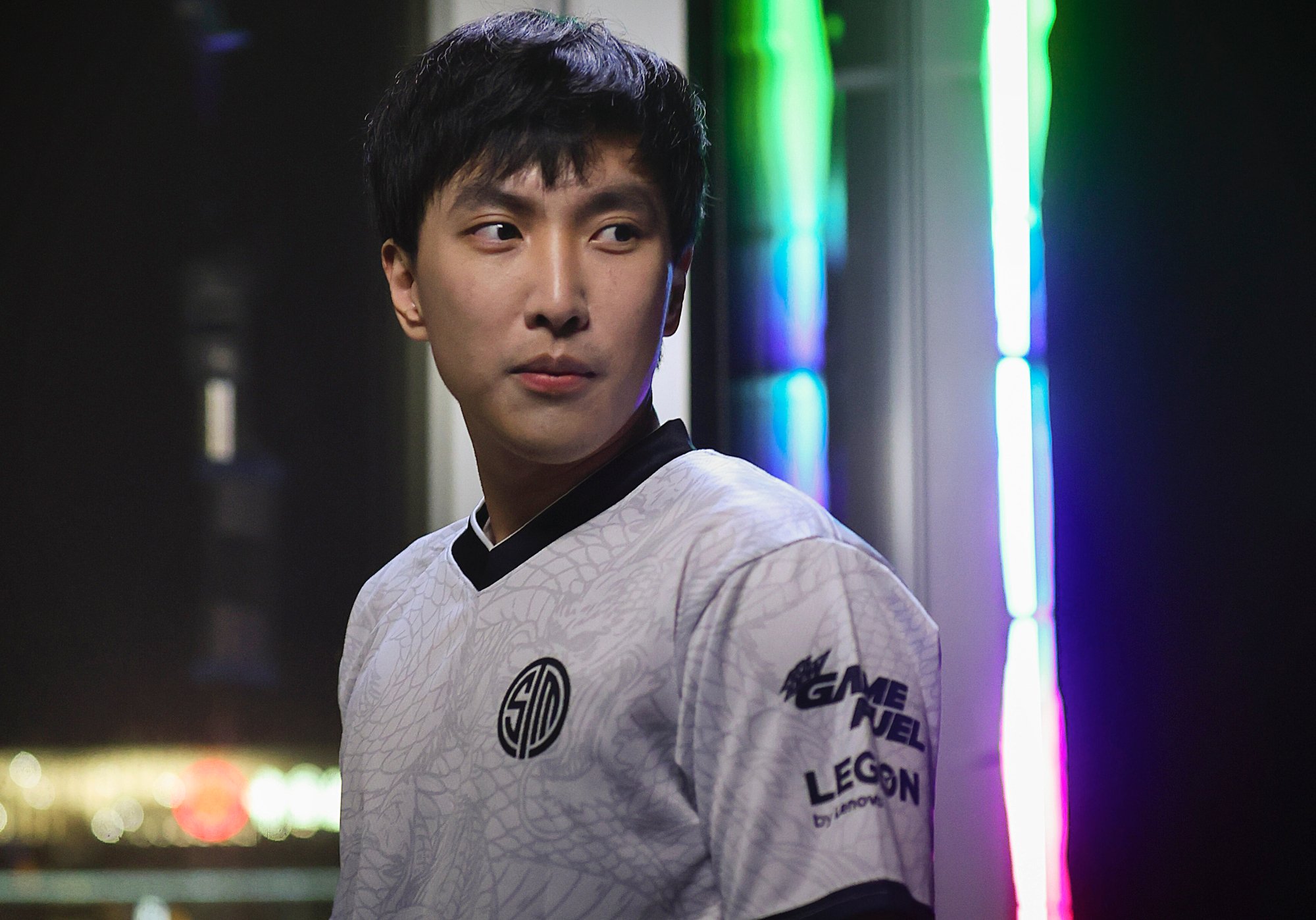 Ex-TSM League of Legends pro player Doublelift, who played under CEO Reginald. He's wearing the TSM jersey and looking to the side in front of neon lights.