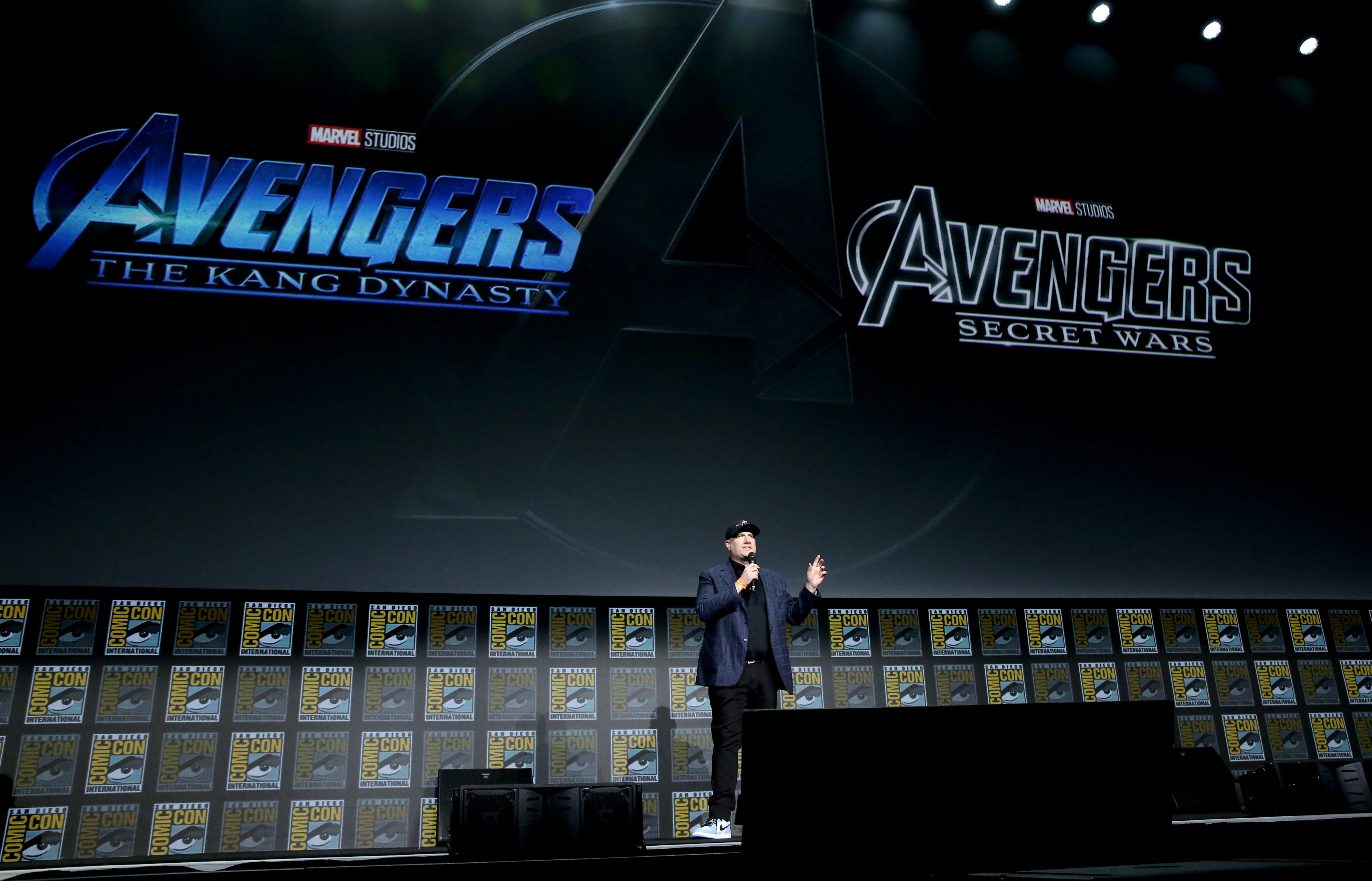 Kevin Feige, who announced 'Fantastic Four' but not the cast at San Diego Comic-Con 2022, stands onstage. Feige wears a dark blue suit over a black shirt, black pants, and a black baseball hat.