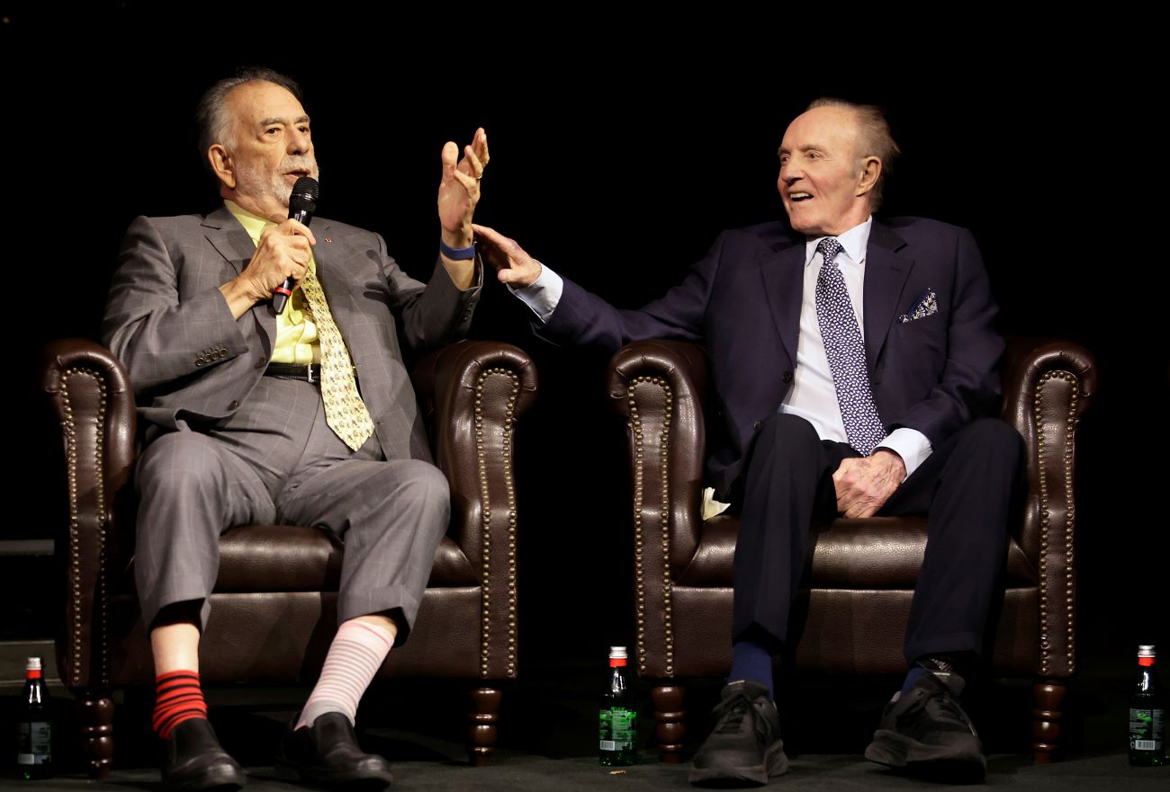 Francis Ford Coppola talks into a microphone and sits next to James Caan. Both sit in armchairs.