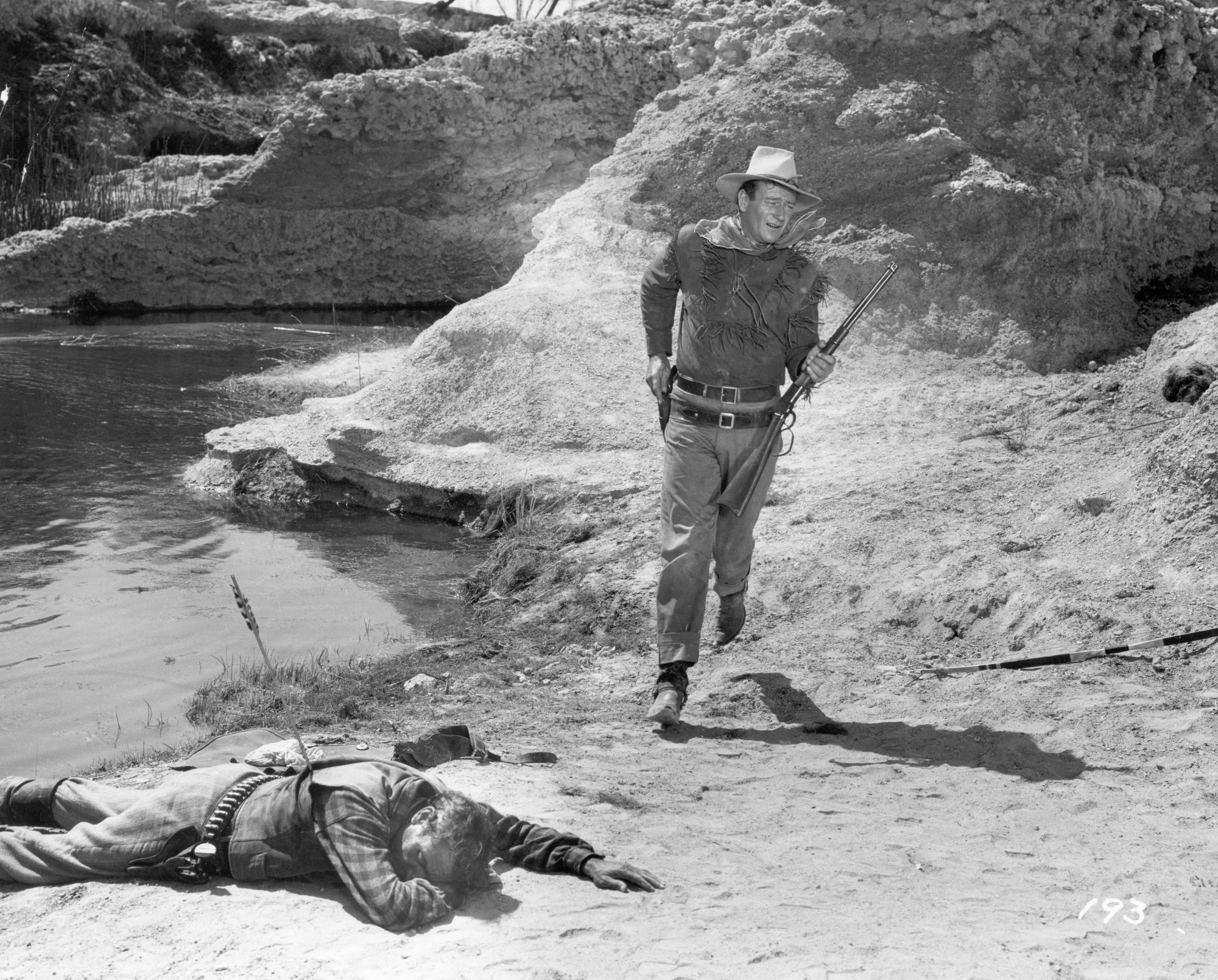 Frank McGrath as Lowe's Partner and John Wayne as Hondo Lane in 'Hondo' movie with McGrath on the ground with an arrow in his back. Wayne walking next to him with Western clothes on.