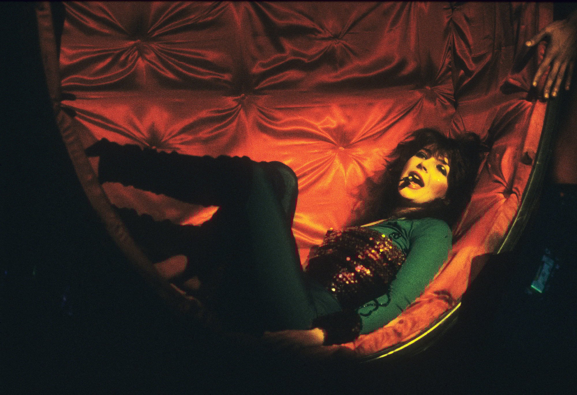 Kate Bush, who sings 'Stranger Things' Season 4's big hit, 'Running Up That Hill.' She's lying on a red chair and singing into a microphone.