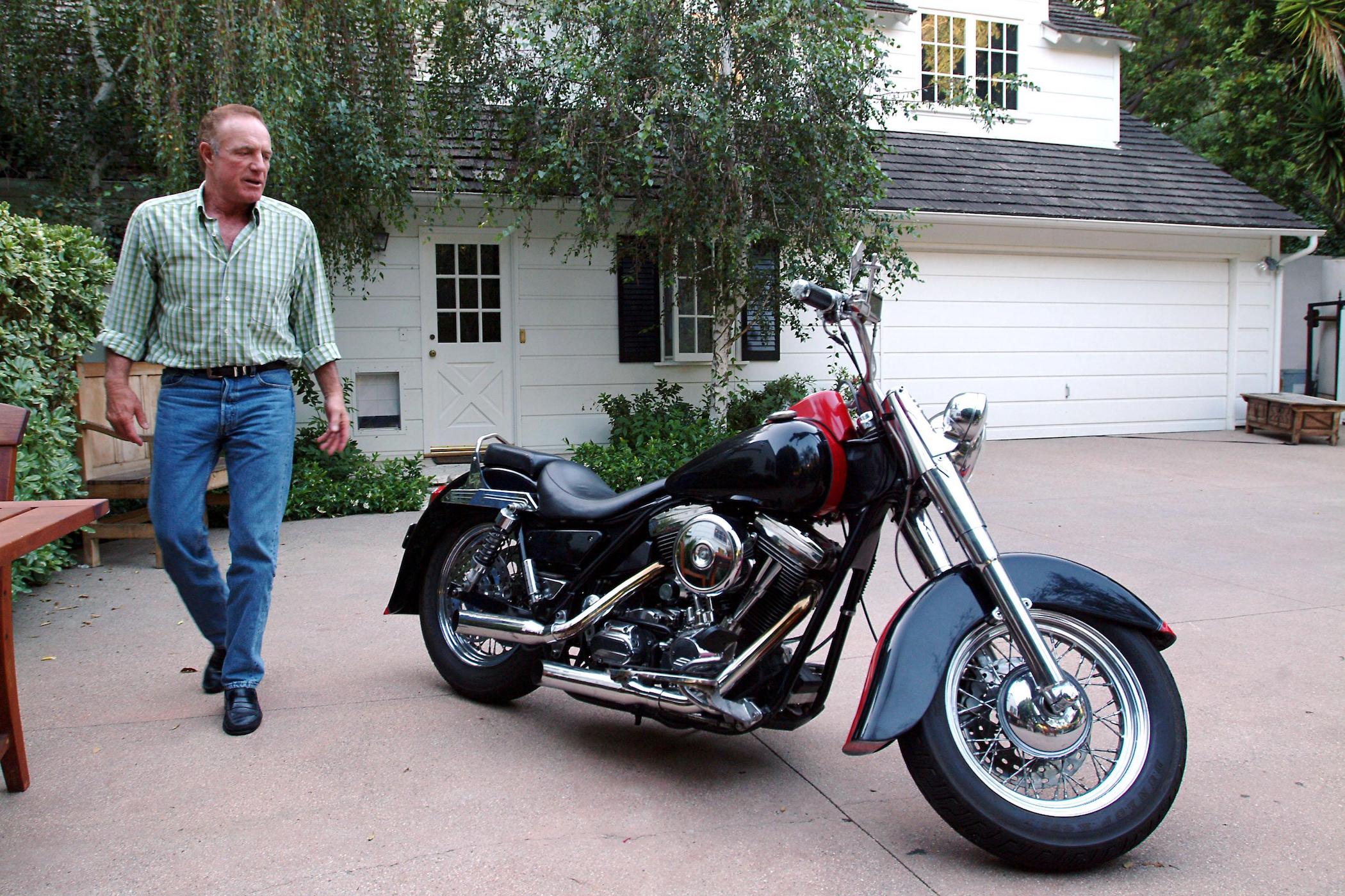 James Caan walking outside of his house next to a parked motorcycle