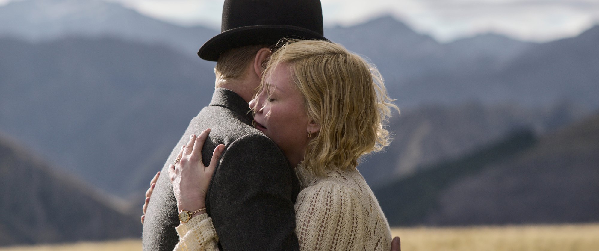 Jane Campion's 'The Power of the Dog' Jesse Plemons as George Burbank and Kirsten Dunst as Rose Gordon embracing each other in Western clothing in front of mountains