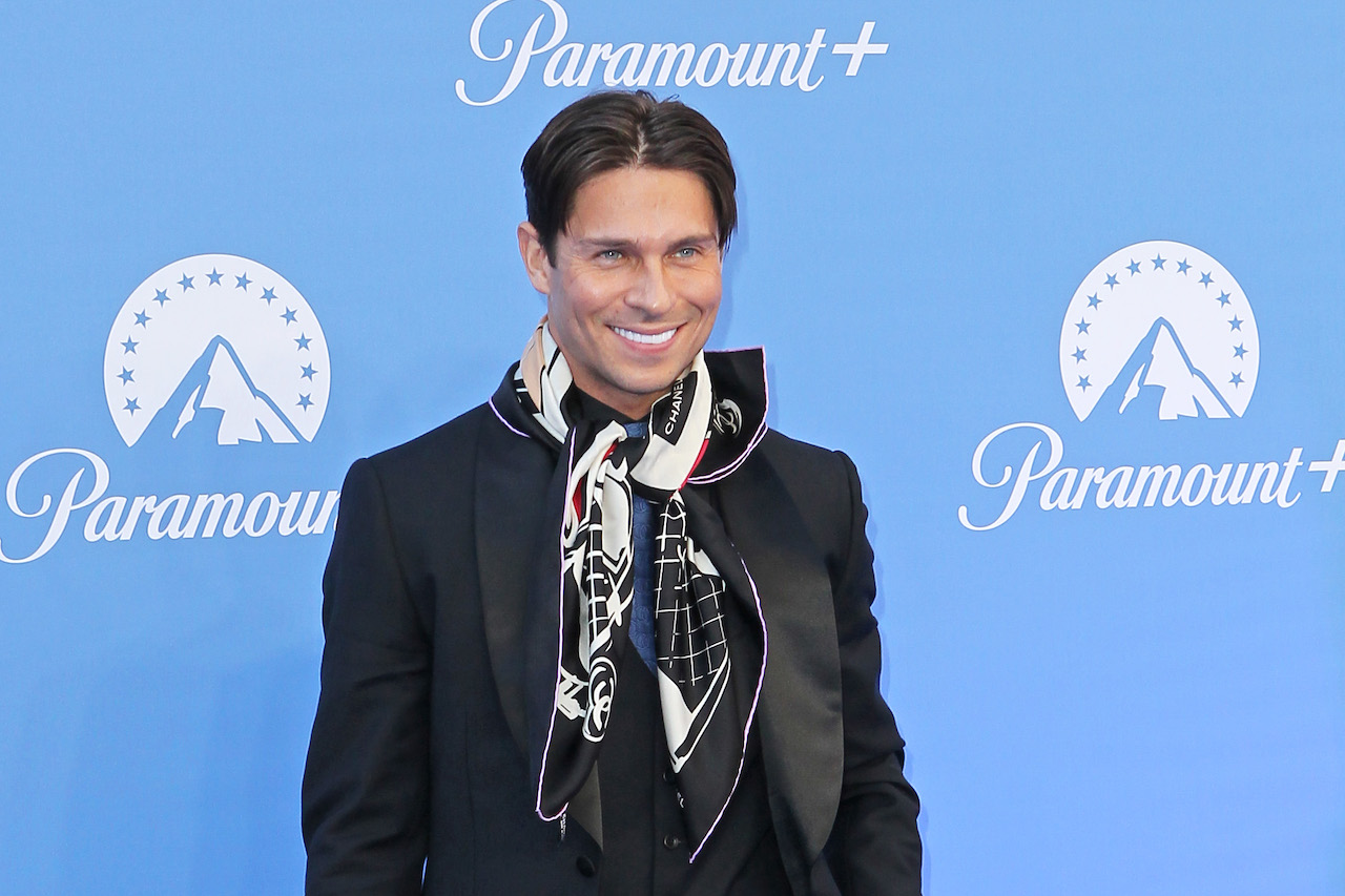 Joey Essex poses in a black suit and big black and white scarf on the red carpet.