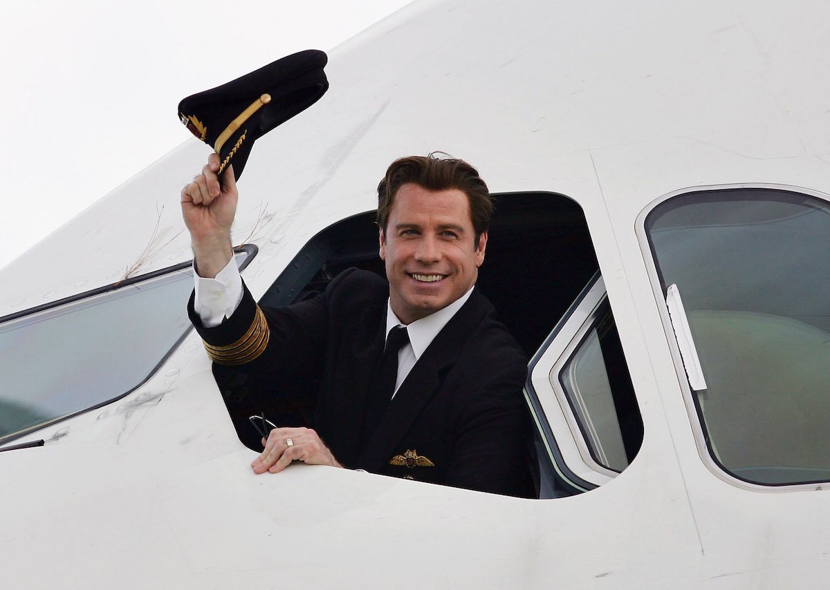 John Travolta waves his pilot hat out of the window of an airplane.