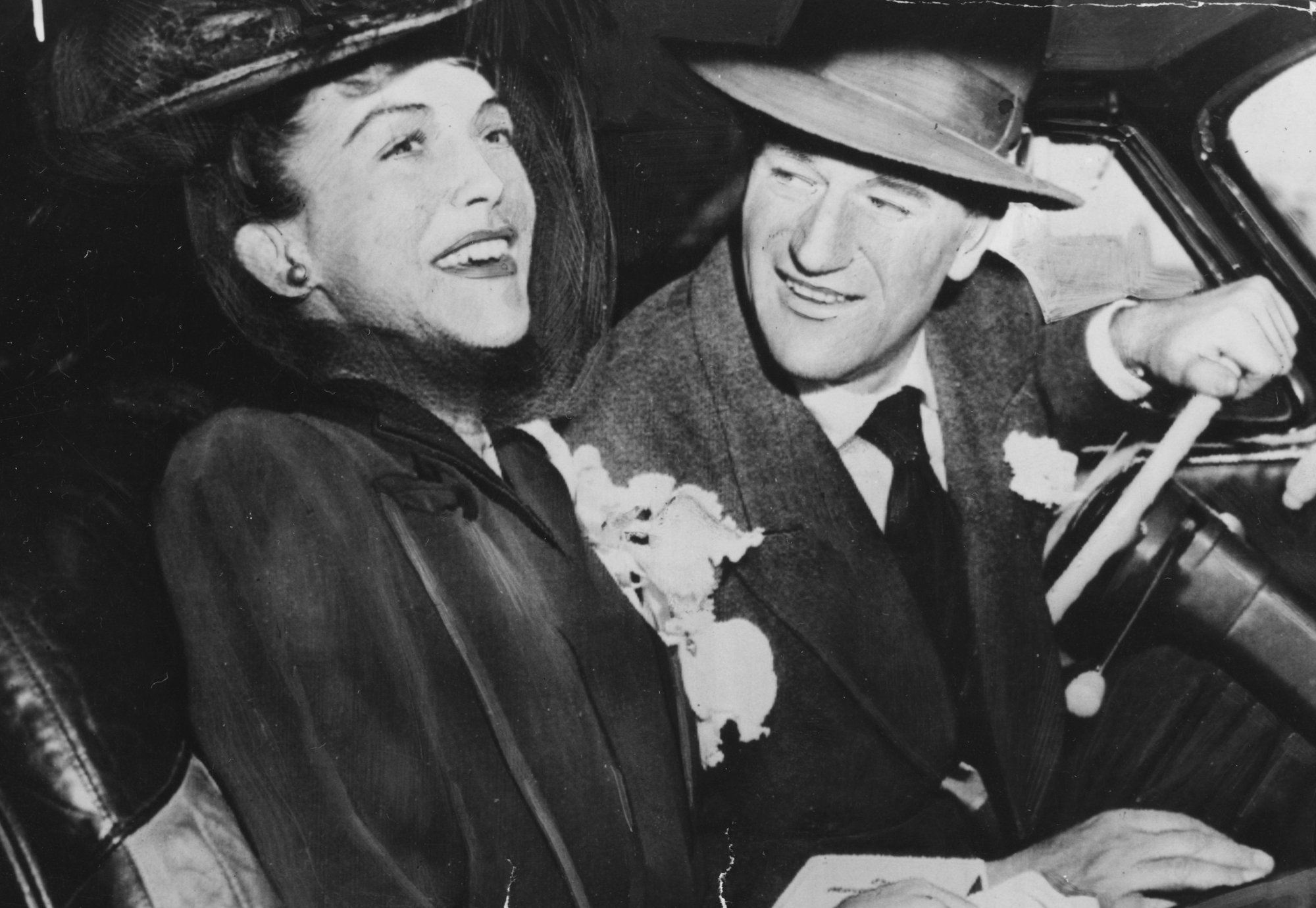 John Wayne and Esperanza Baur, the second wife over the course of his life smiling sitting in a car wearing hats