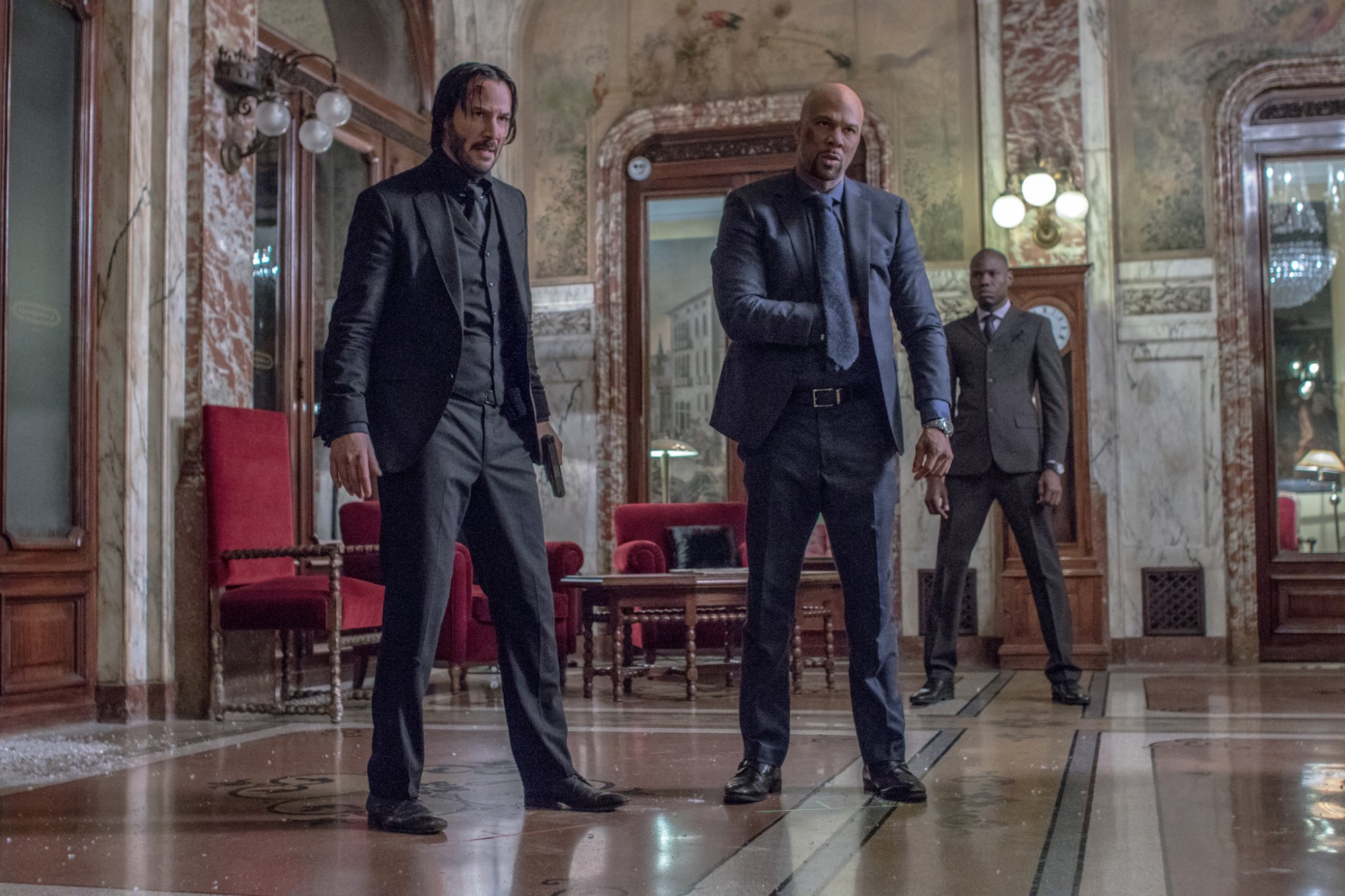 'John Wick 2' Keanu Reeves as John Wick and Common as Cassian wearing suits covered in bruises in a grand room with broken glass on the floor