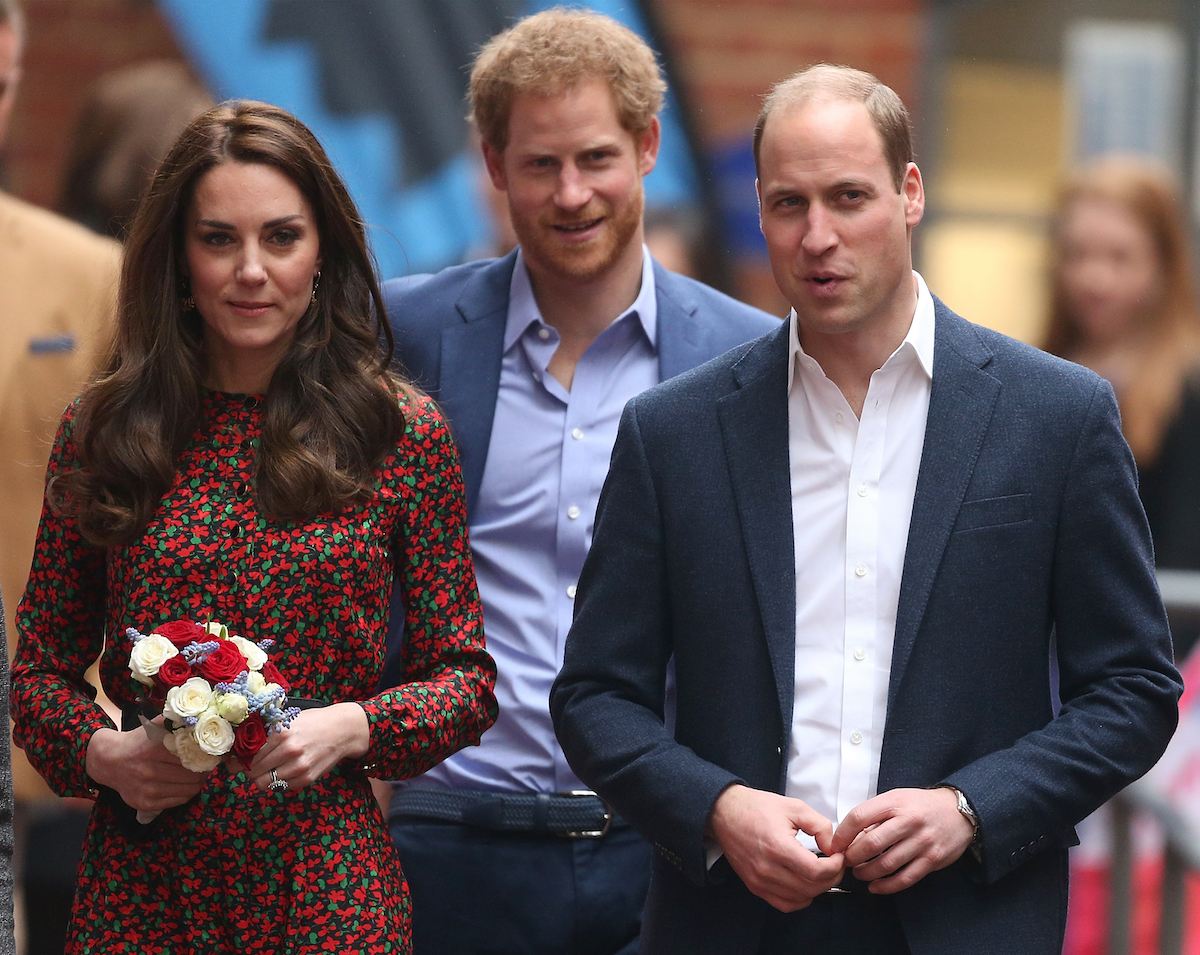 Kate Middleton and Prince William, who, according to Omid Scobie are considering visiting the U.S. more, stand with Prince Harry