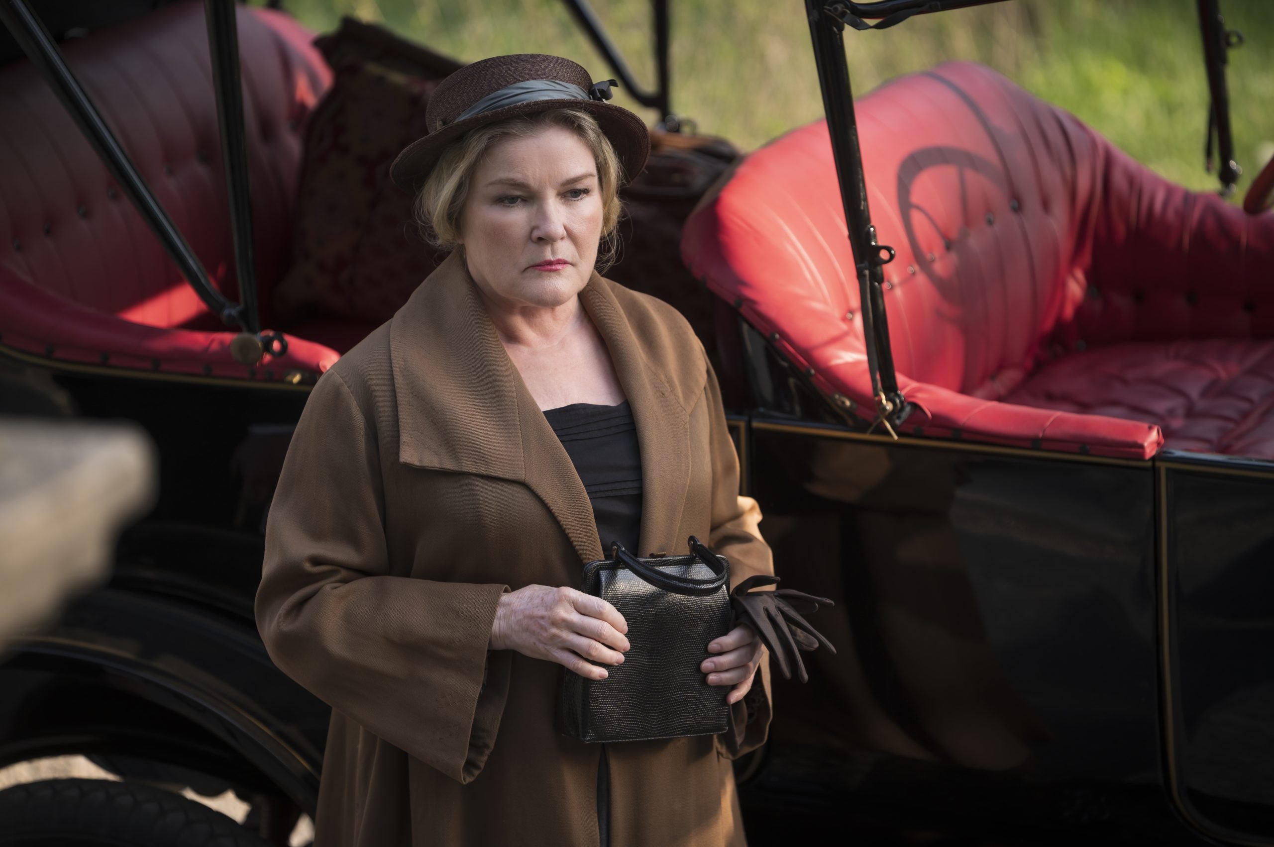 Kate Mulgrew as Mrs. Steiner, wearing a hat and standing in front of a car in 'Flowers in the Attic: The Origin'