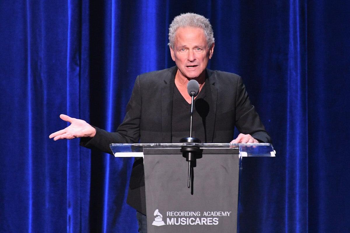 Lindsey Buckingham, member of Fleetwood Mac with Christine McVie, speaks into a microphone at an event.
