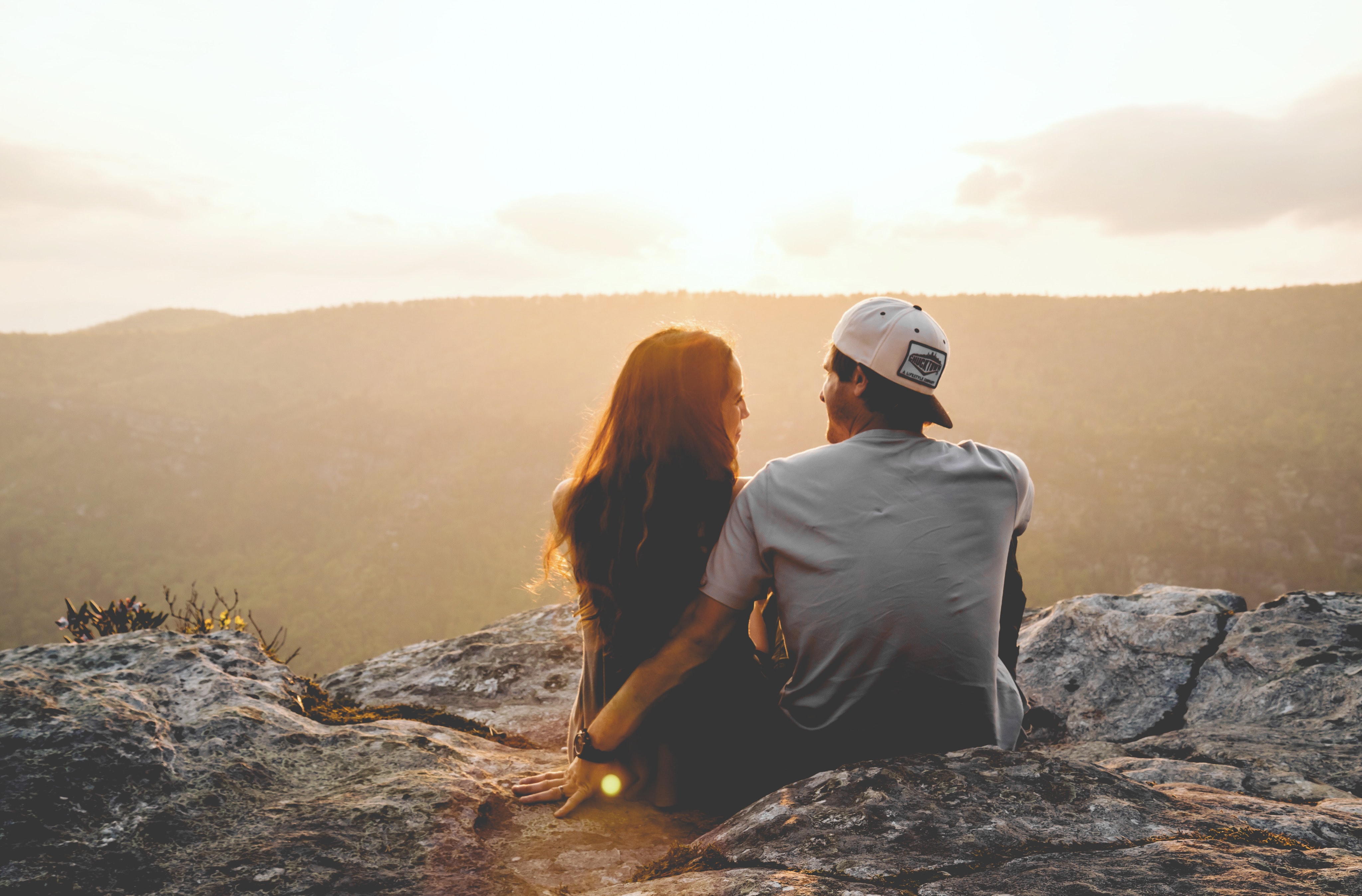 A couple sits on a rock while the sun sets.