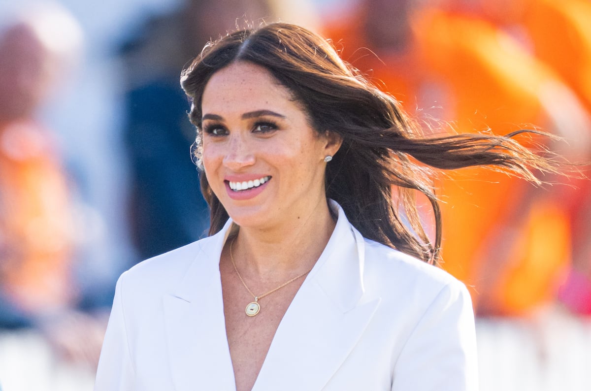 Meghan Markle, who hinted at a trip to Washington, D.C., after the U.S. Supreme Court overturned Roe v. Wade, smiles and looks on wearing a white suit