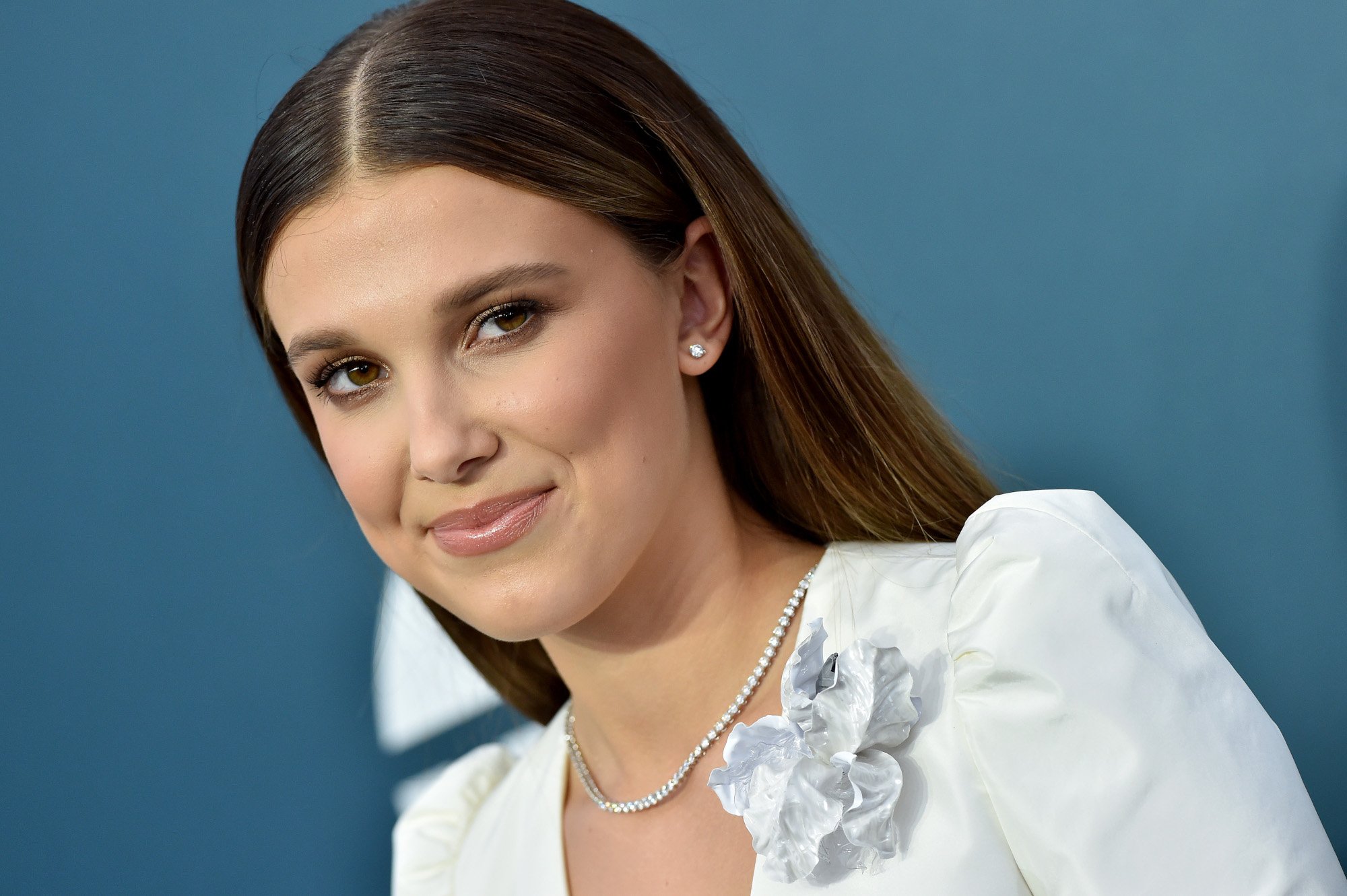Millie Bobby Brown, who is rumored to be in talks for a 'Star Wars' movie or show. She's wearing a white dress, her hair is brown and straight, and she's smiling.