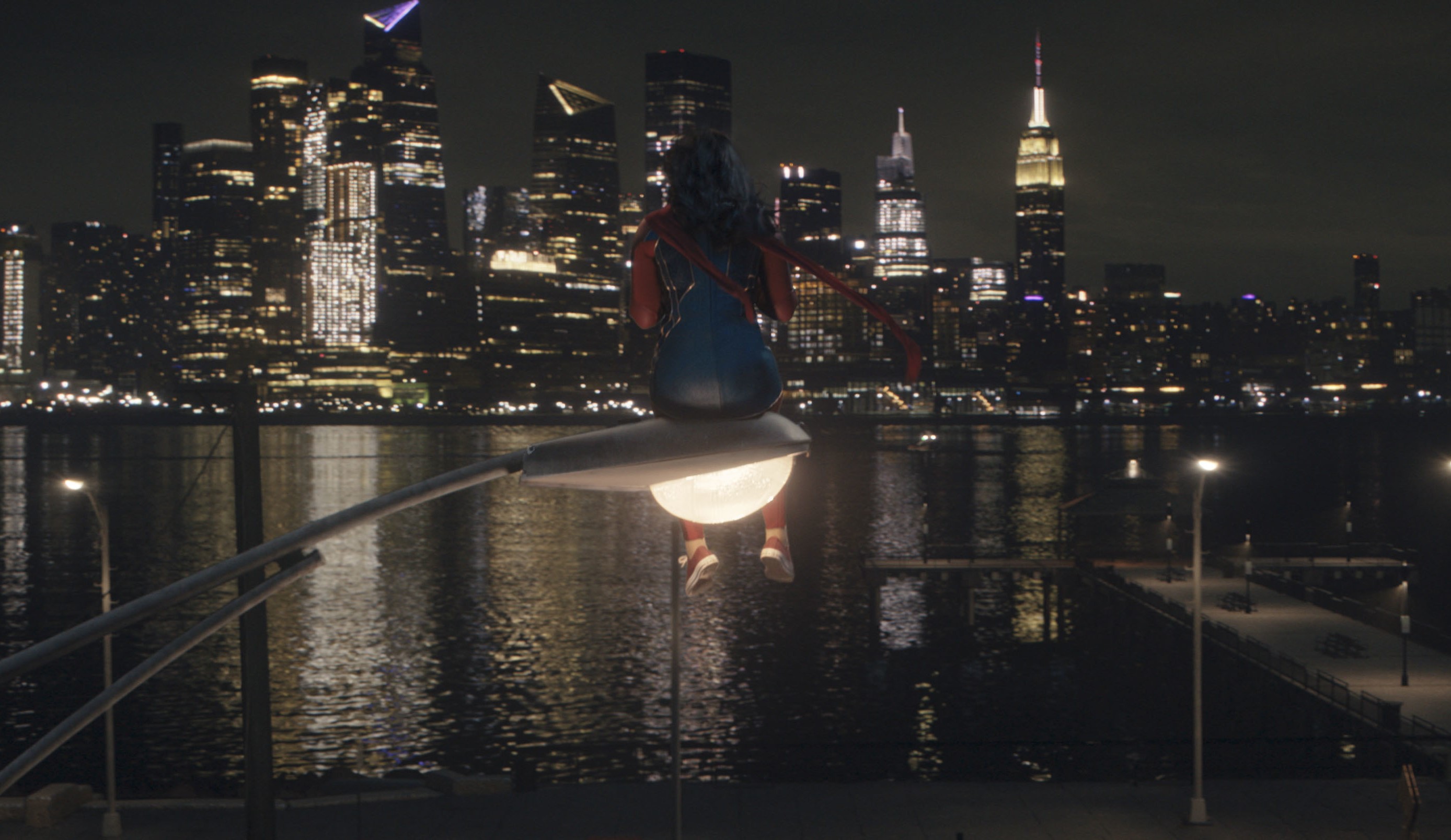 Iman Vellani as Kamala Khan in 'Ms. Marvel,' which streams its finale with episode 6. She's sitting on a street light and staring out at a city landscape.