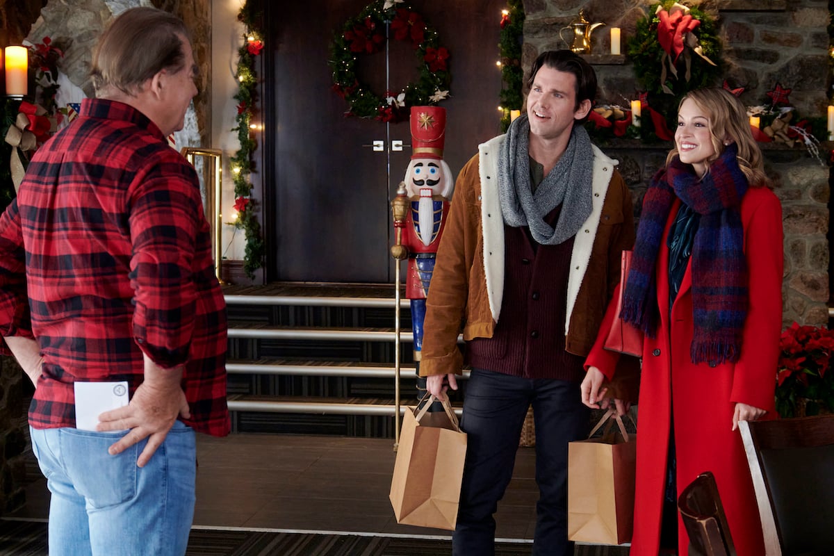 Man in a checked shirt facing Kevin McGarry and Kayla Wallace, holding shopping bags, in the Hallmark Channel movie 'My Grown-Up Christmas List'