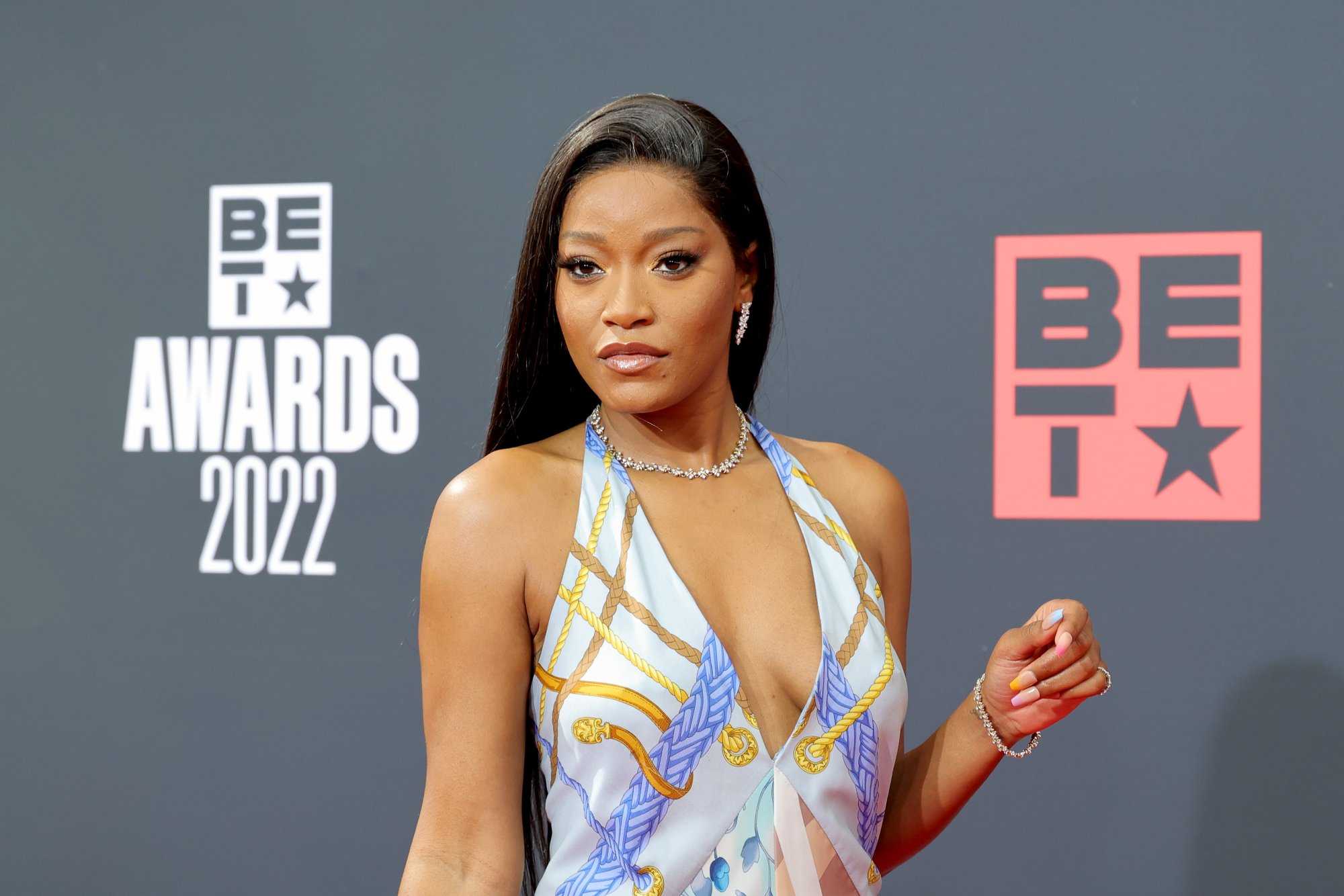 'Nope' actor Keke Palmer, who was compared to Zendaya wearing a white, blue, and gold dress with multicolored fingernails. She's standing in front of the BET Awards 2022 step and repeat.