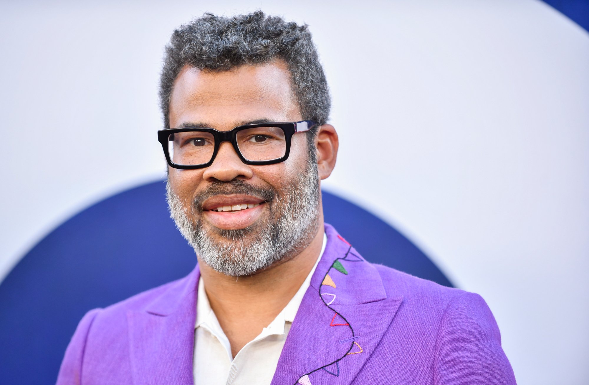 'Nope' filmmaker Jordan Peele smiling while wearing a purple suit jacket