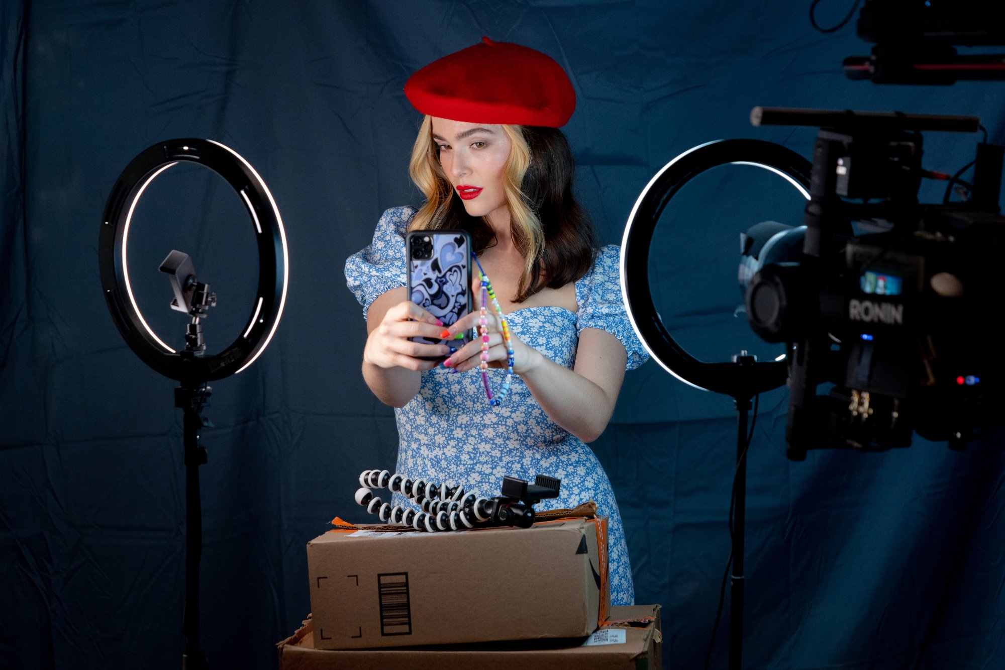 'Not Okay' Zoey Deutch as Danni Sanders taking a selfie on her iPhone wearing a red hat in front of a blank background with ring lights lighting her up