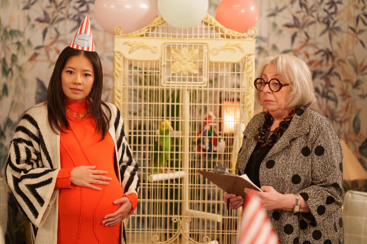 Nina Lin and Bunny in Only Murders in the Building Season 2. Nina wears a party hat. She and Bunny stand in front of a bird cage.