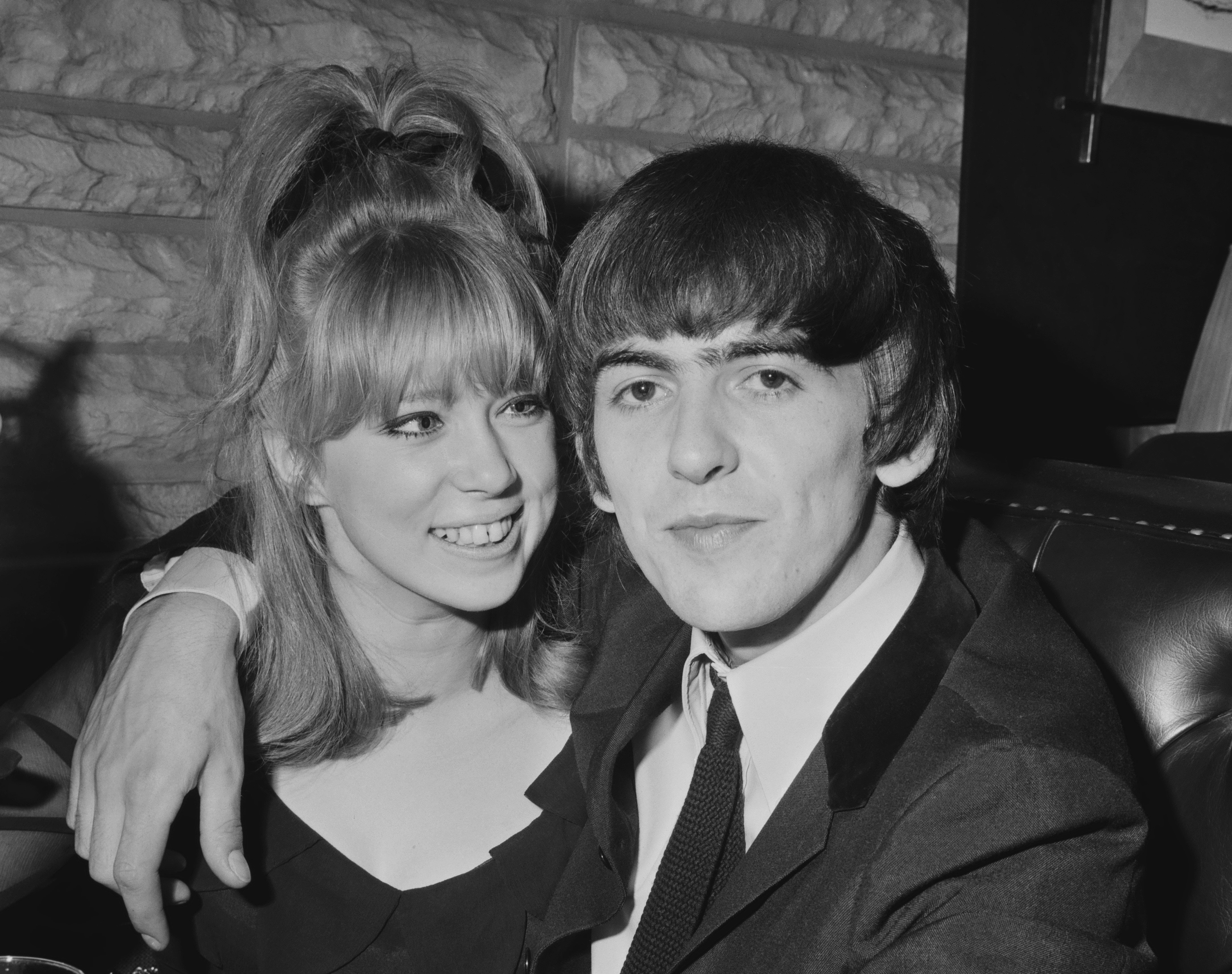 A black and white picture of George Harrison with his arm around Pattie Boyd's shoulder. 