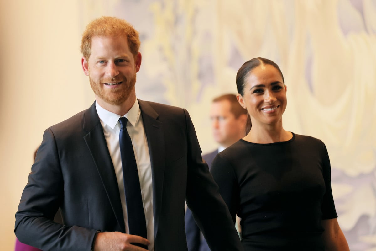 Memoir author Prince Harry and Meghan Markle body language looks supportive as they smile and hold hands at an event