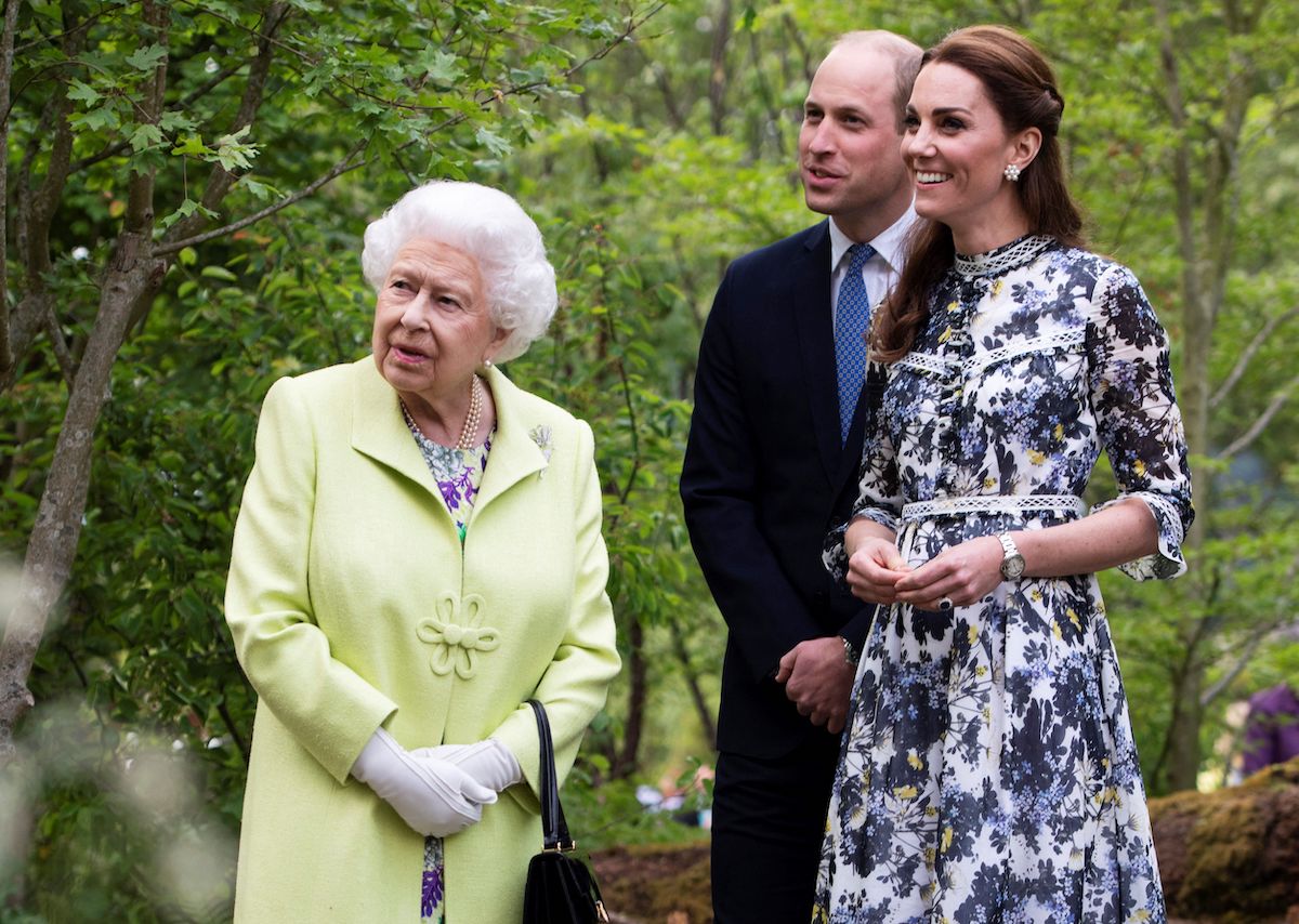 Queen Elizabeth II, who a royal commentator says will 'summon' Kate Middleton and Prince William because of their helicopter use, stands with Prince William and Kate Middleton in a garden
