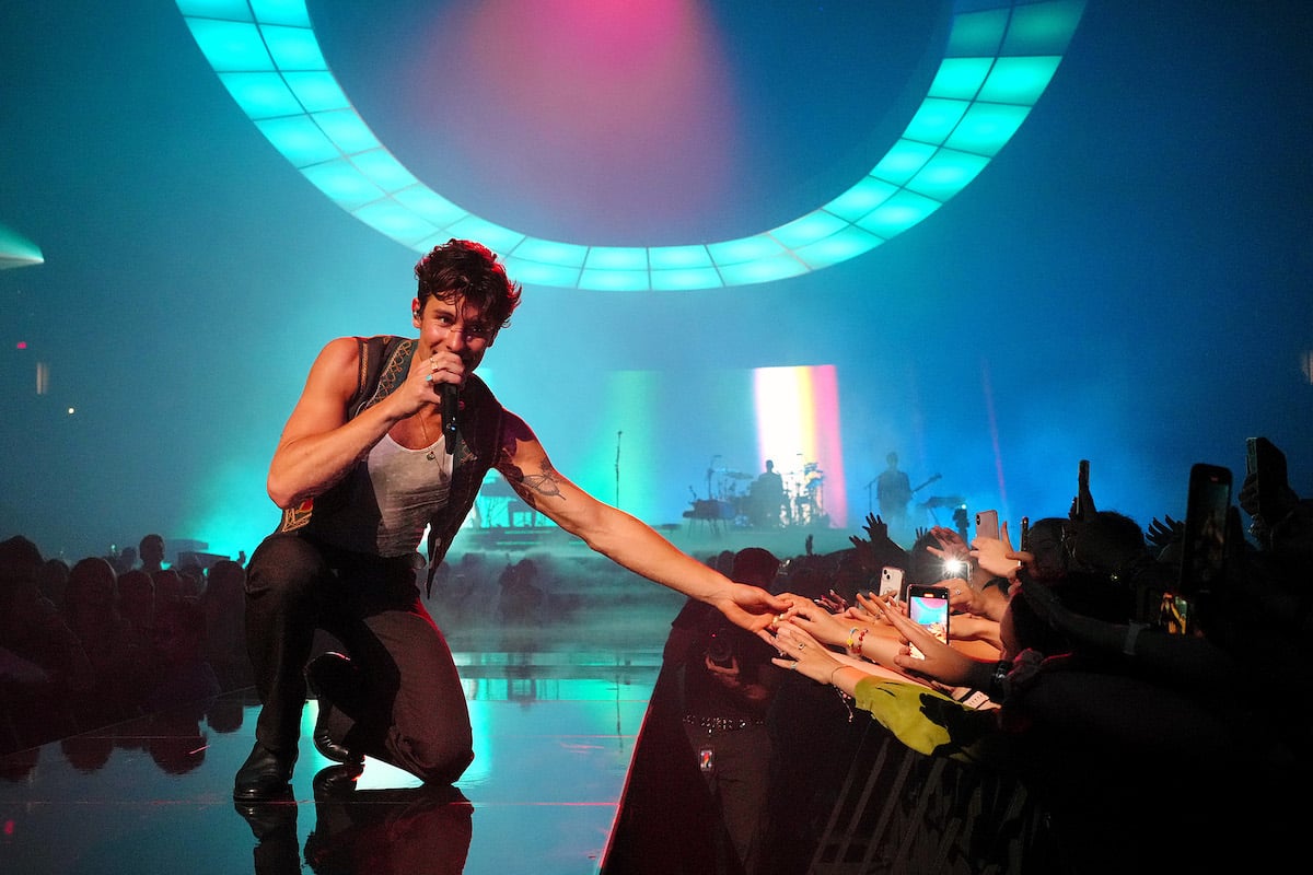 Shawn Mendes performs on stage while reaching out to touch fans' hands.