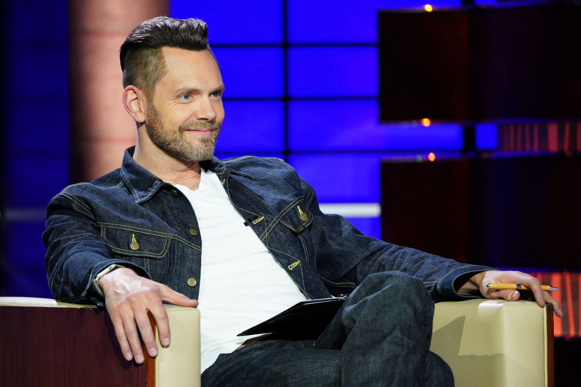 Joel McHale, who is in the 'Stargirl' Season 3 trailer, wears a dark blue jean jacket over a white shirt and jeans.