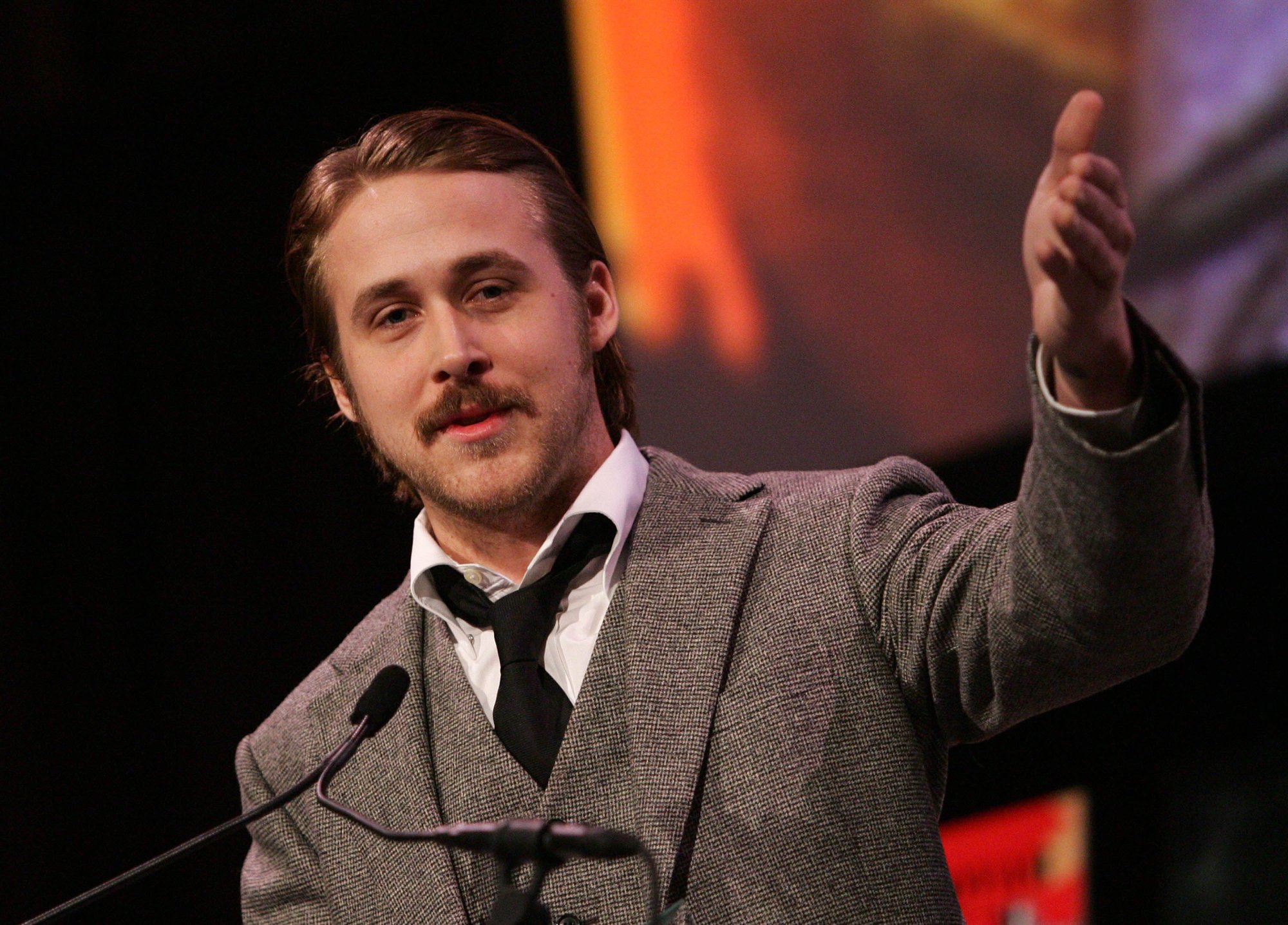 'Stay' movie star Ryan Gosling wearing a tan suit and tie, holding his hand up and talking into a microphone