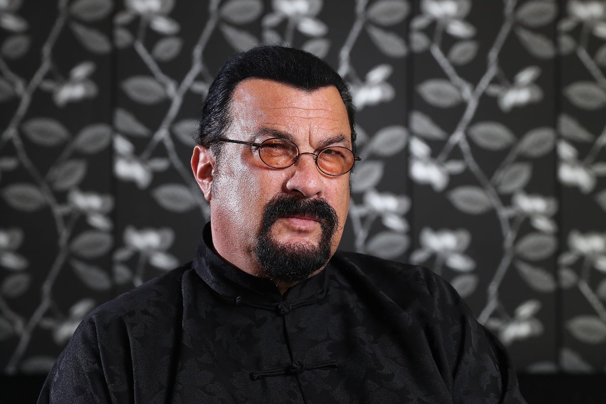 Steven Seagal sitting down while wearing black clothes.