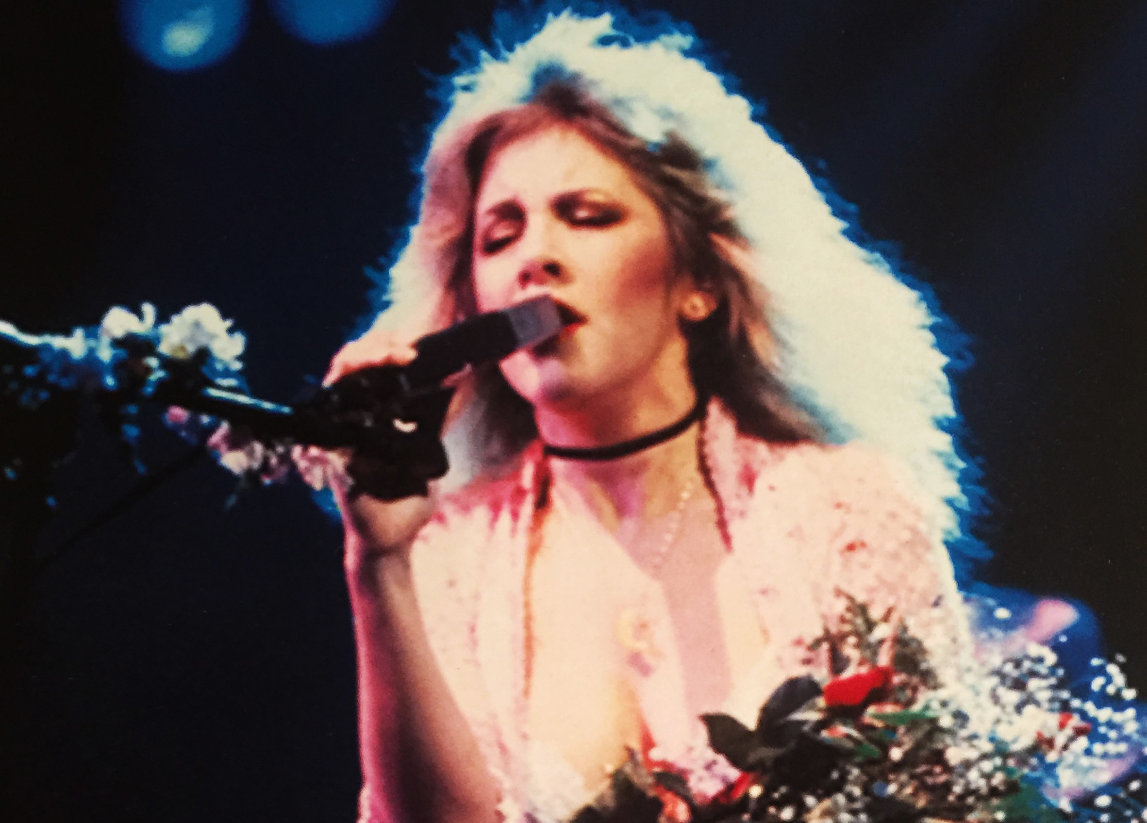 Stevie Nicks sings into a microphone and holds a bouquet of flowers.