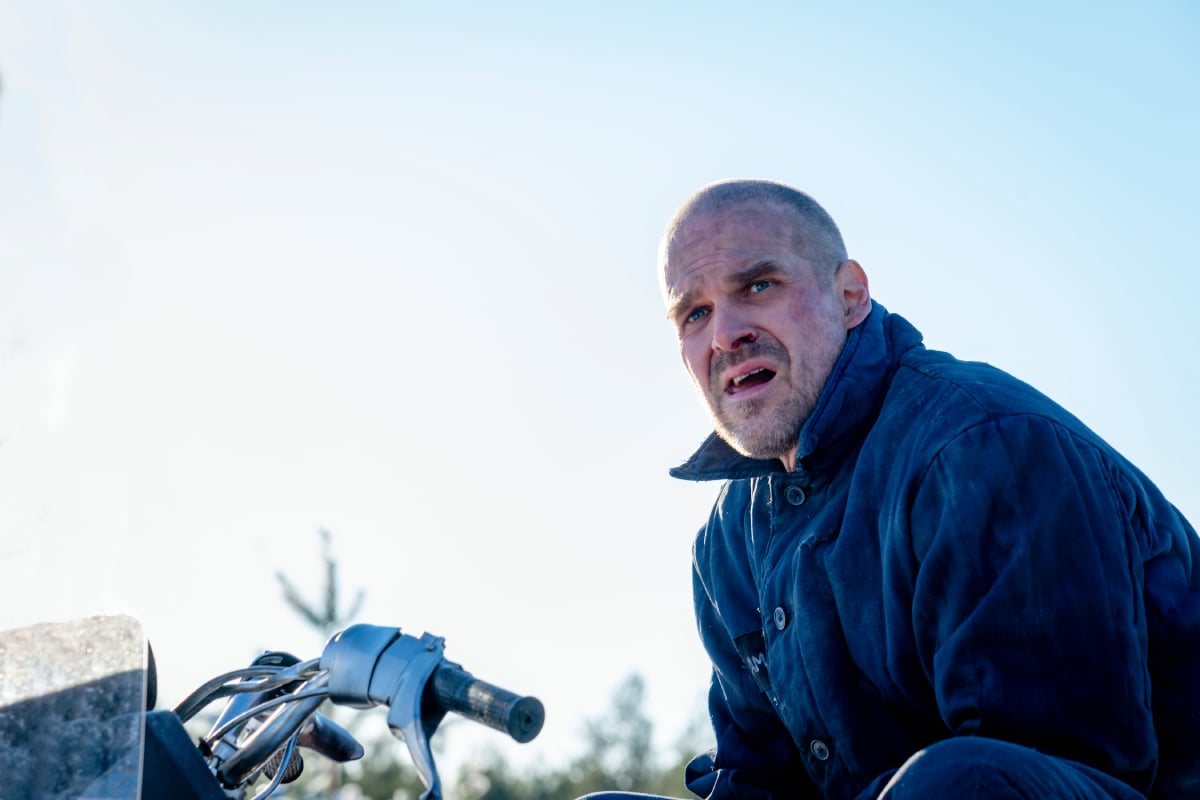 David Harbour as Jim Hopper in Stranger Things. Jim sits on top of a snow mobile in Russia.