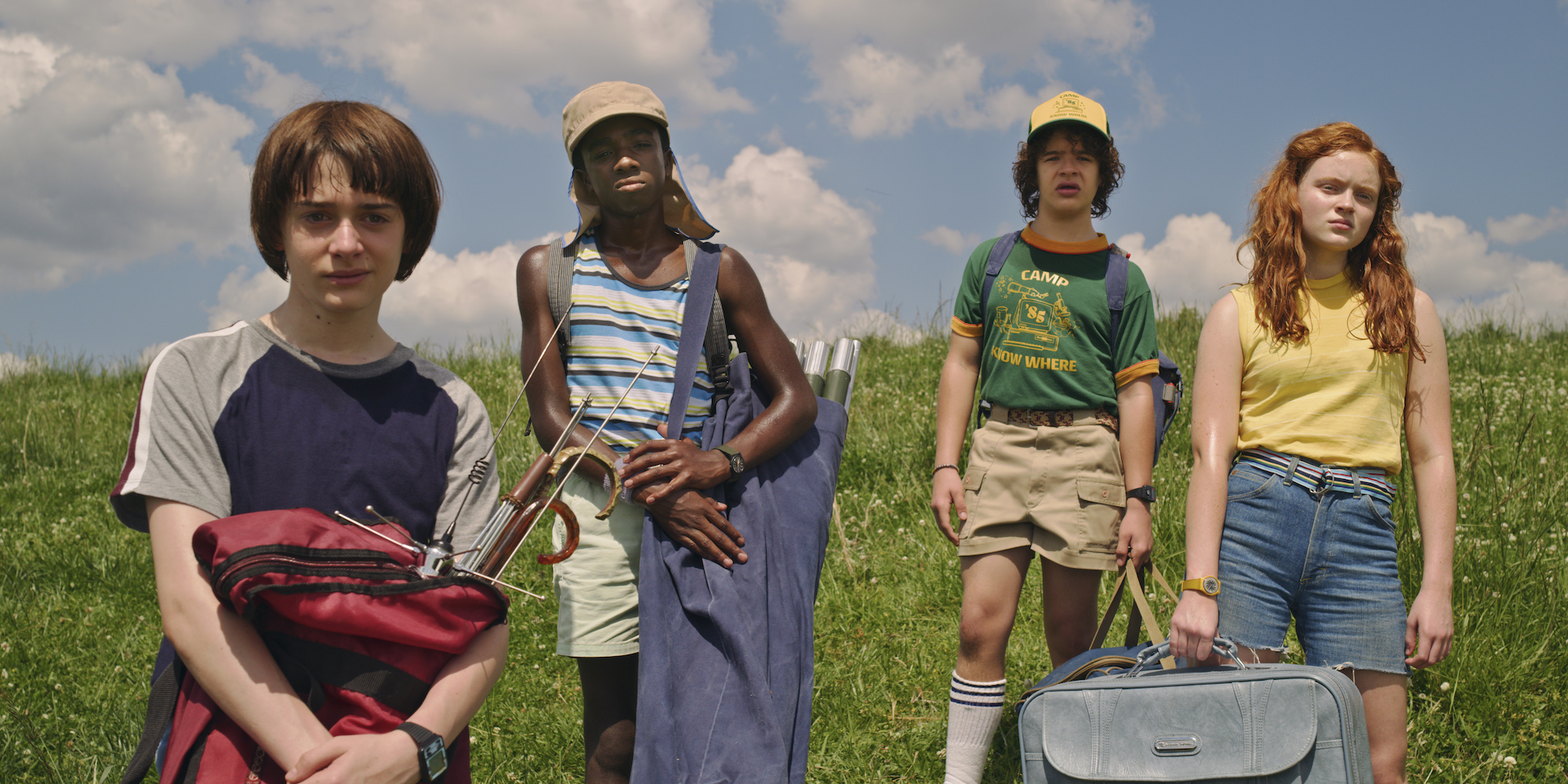 'Stranger Things' Season 3 production still showing Noah Schnapp, Caleb McLaughlin, Gaten Matarazzo, and Sadie Sink standing in a field. This season is a perfect summer show.