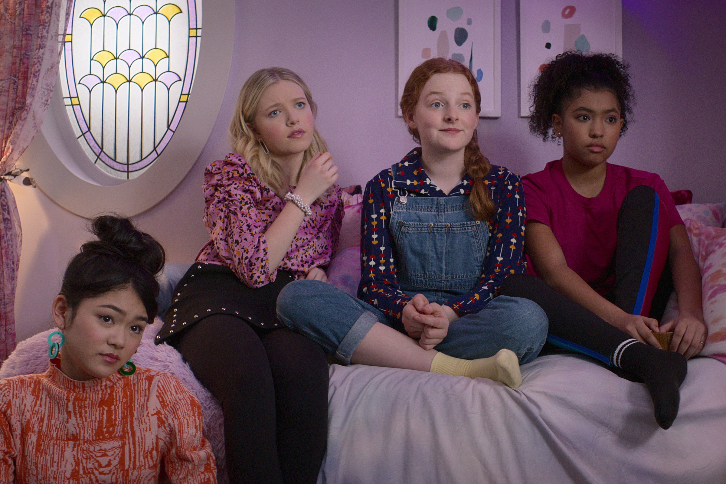 Momona Tamada, Shay Rudolph, Vivian Watson, and Anais Lee in 'The Baby-Sitter's Club,' one of Netflix's canceled shows of 2022. The four are sitting on or next to a bed and looking at something off-screen.