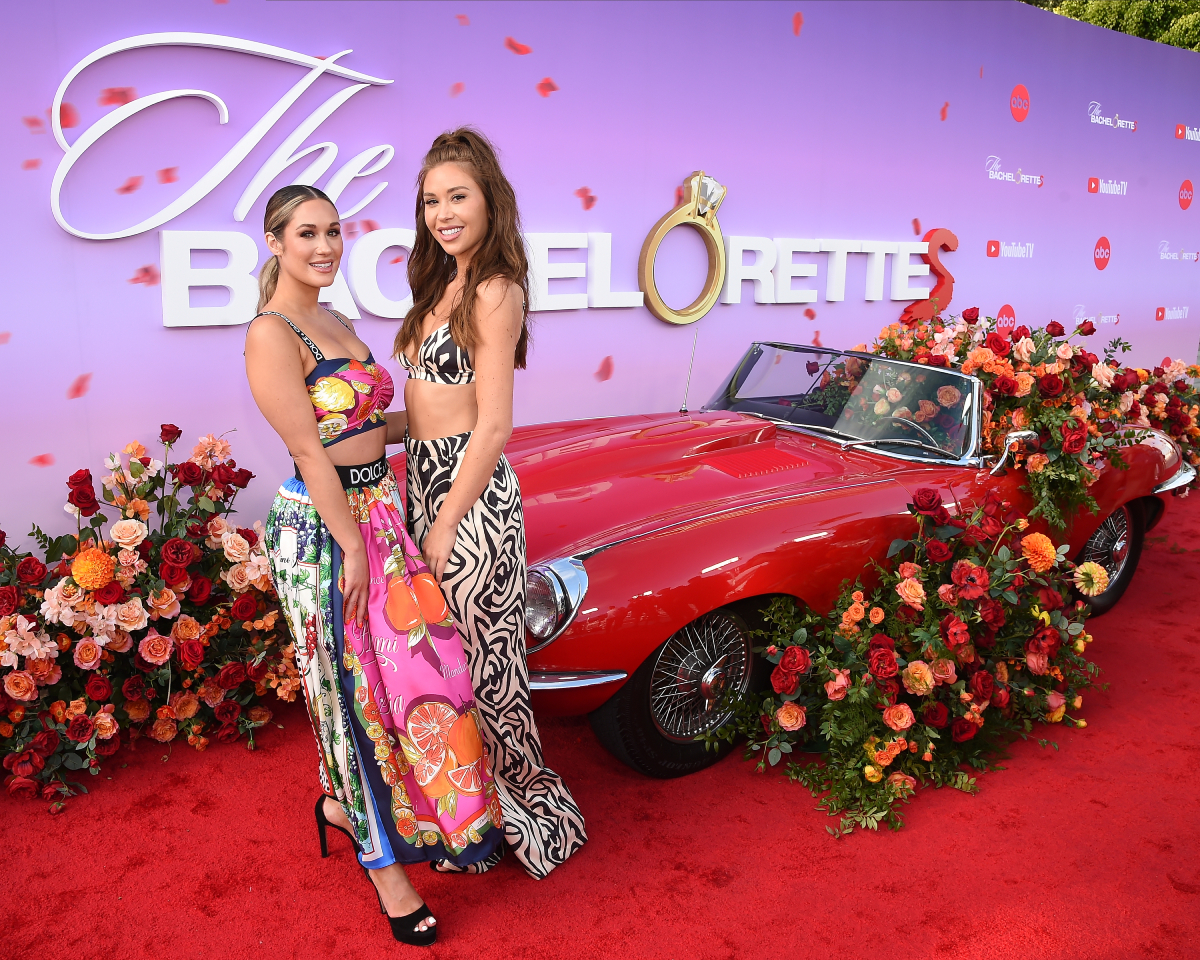 The Bachelorette 2022 has several filming locations. Gabby and Rachel pose in front of a red car full of flowers. 