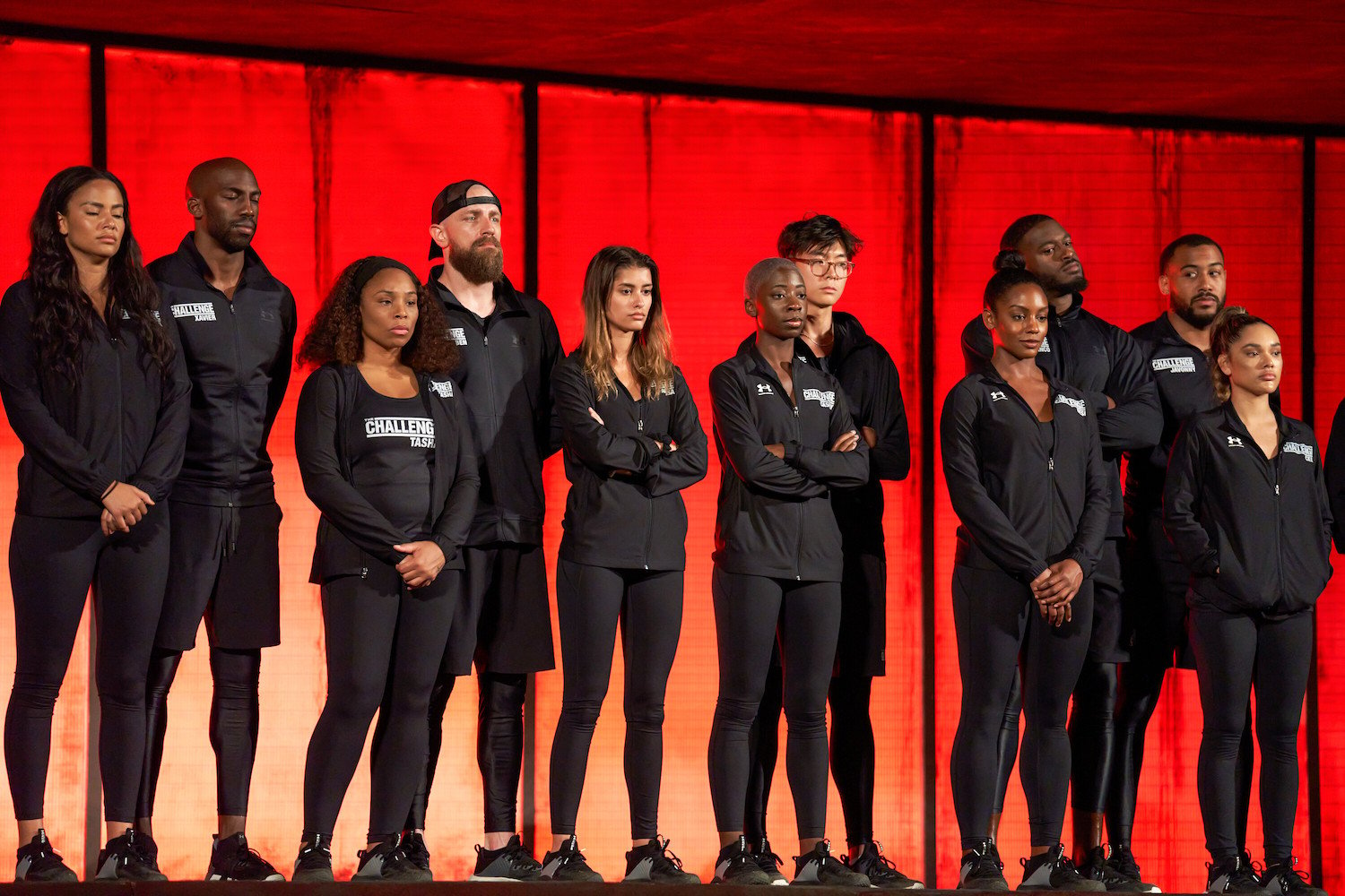 The cast of 'The Challenge: USA' standing together in black against a red background
