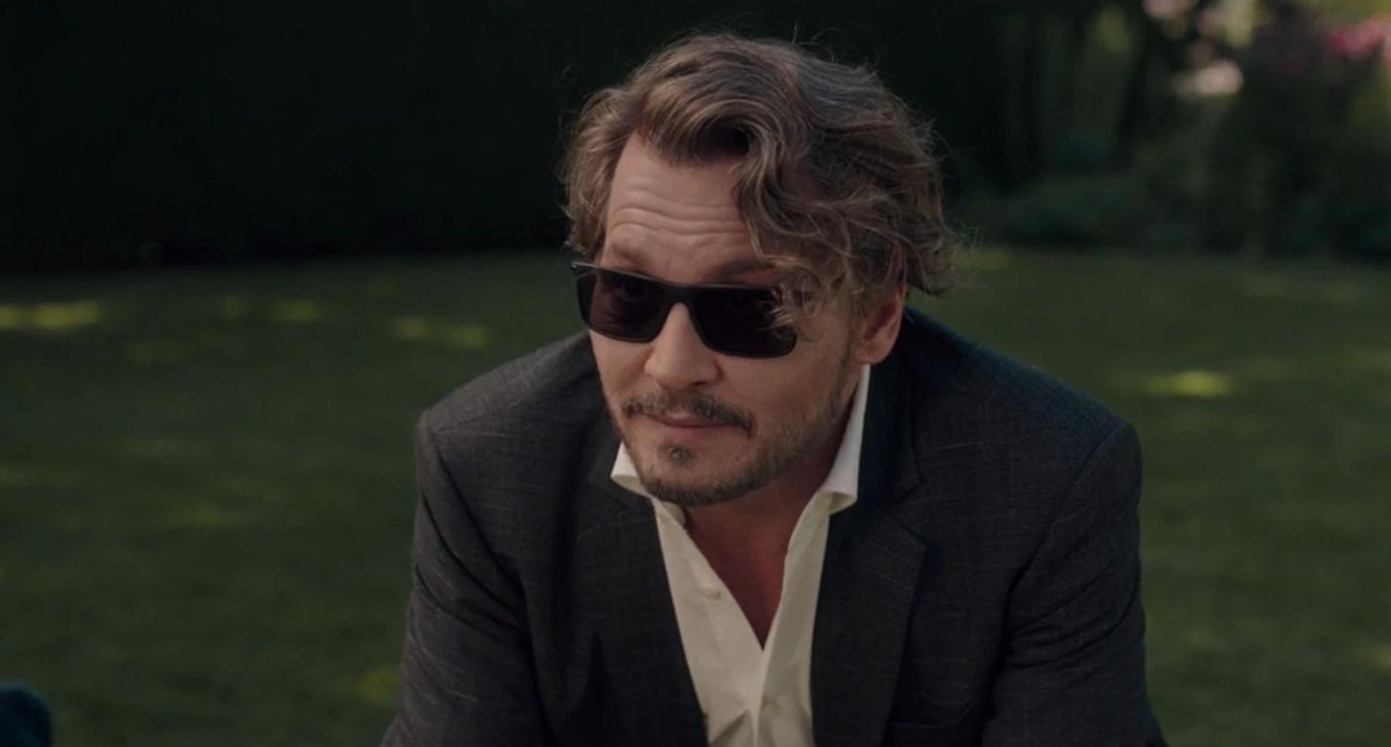 'The Professor' Johnny Depp as Richard in 2018 movie wearing sunglasses and a suit with grass in the background