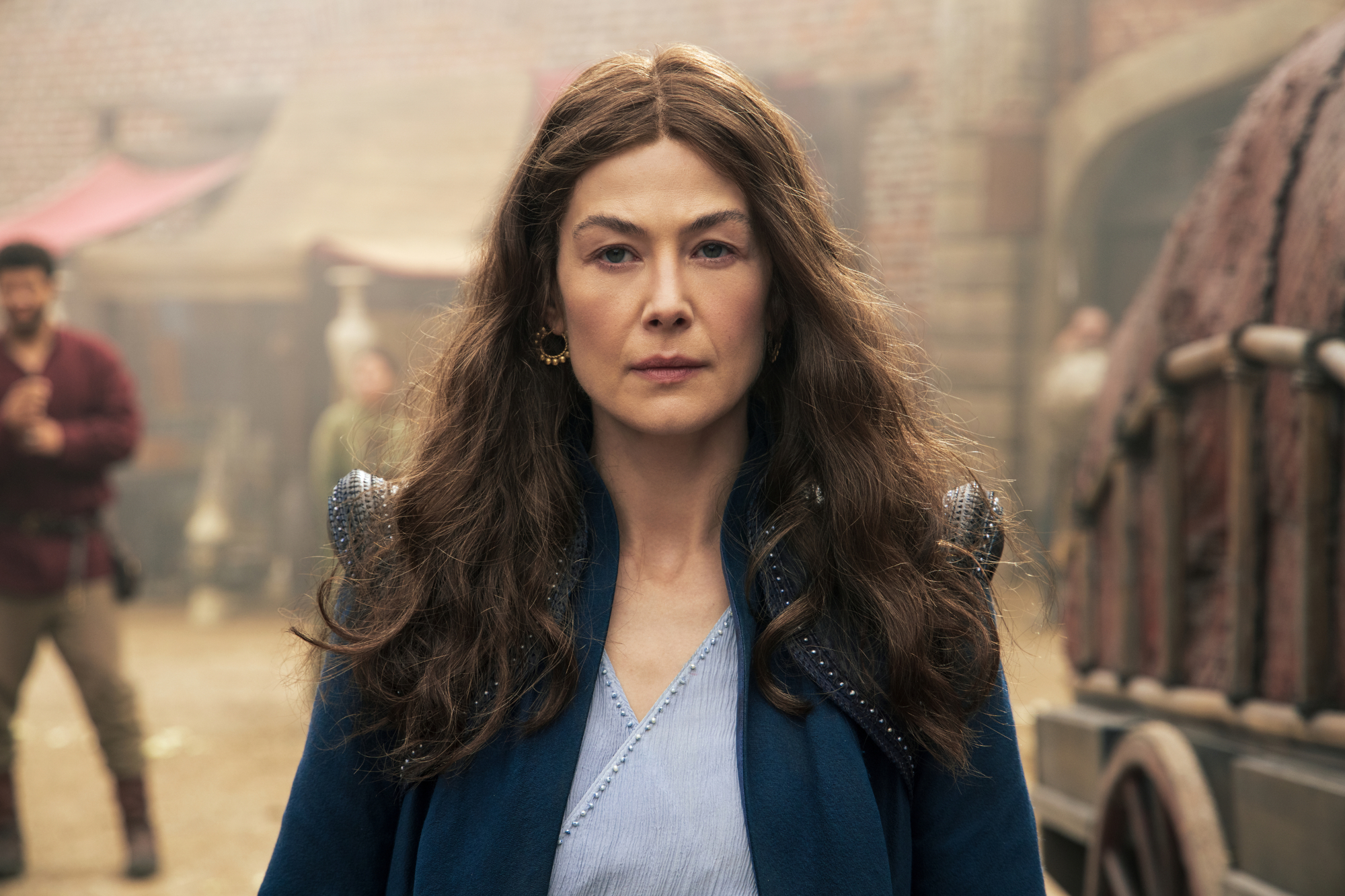 Rosamund Pike as Moiraine Damodred in 'The Wheel of Time,' which will receive a season 2 on Prime Video. She's staring directly at the camera, and there's a town behind her.