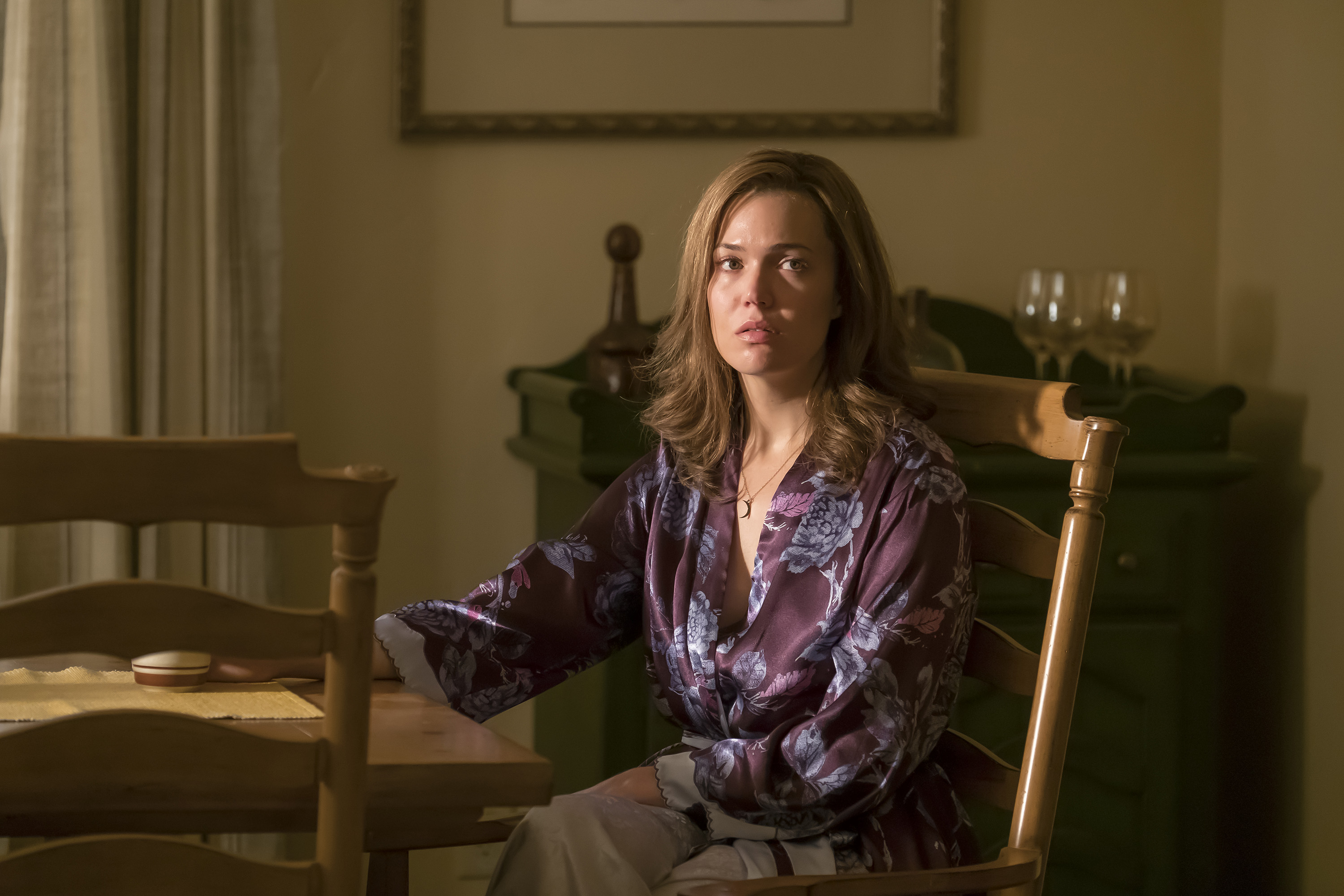 Mandy Moore, in character as Rebecca Pearson in 'This Is Us' Season 1, sits at the dining room table wearing a purple robe with blue flowers on it.