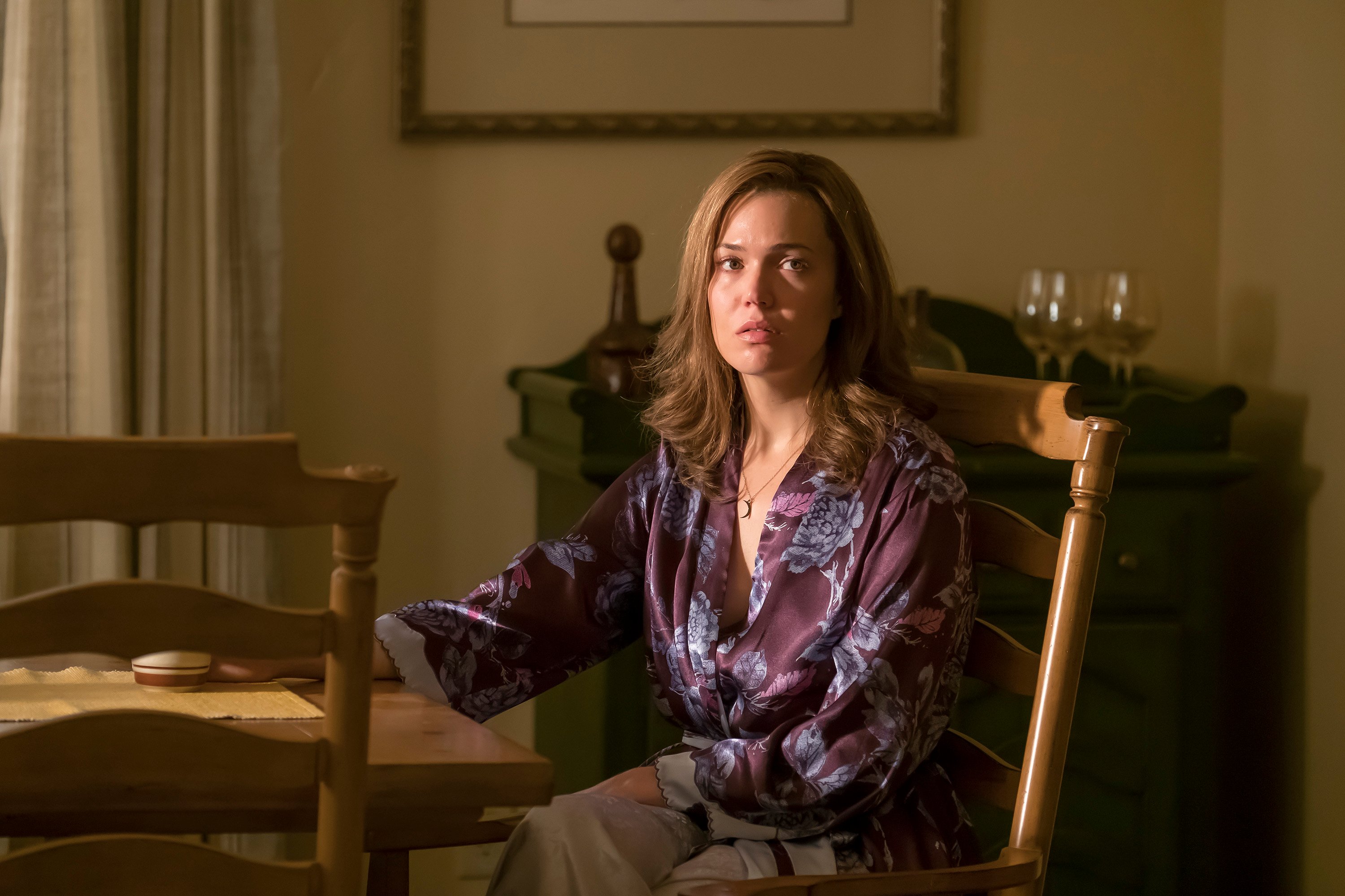 Mandy Moore, in character as Rebecca Pearson in 'This Is Us' Season 1, sits at the dining room table wearing a purple robe with blue flowers on it.