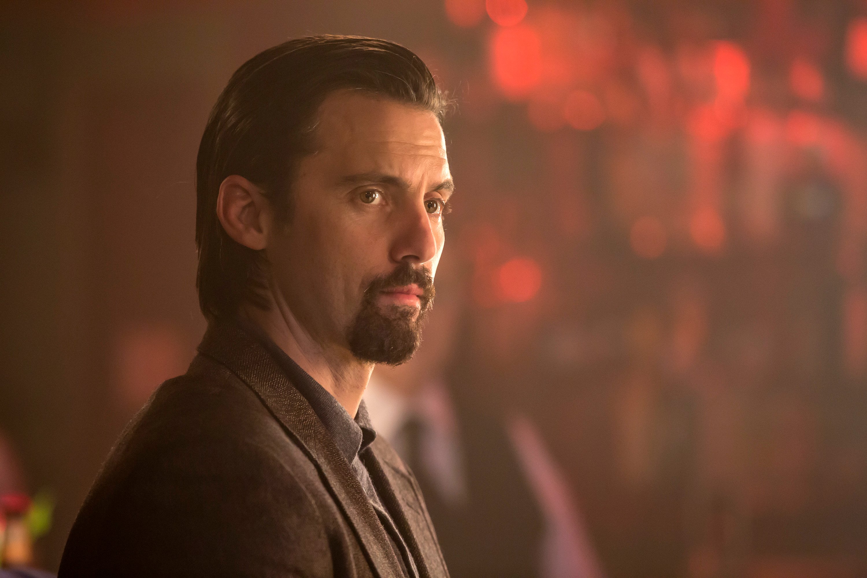 Milo Ventimiglia, in character as Jack in 'This Is Us' Season 1, wears a dark brown suit over a gray collared shirt.