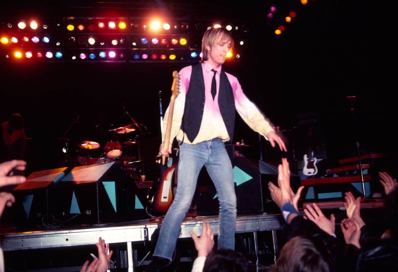 Tom Petty holds a guitar and reaches out to touch his fans' hands.