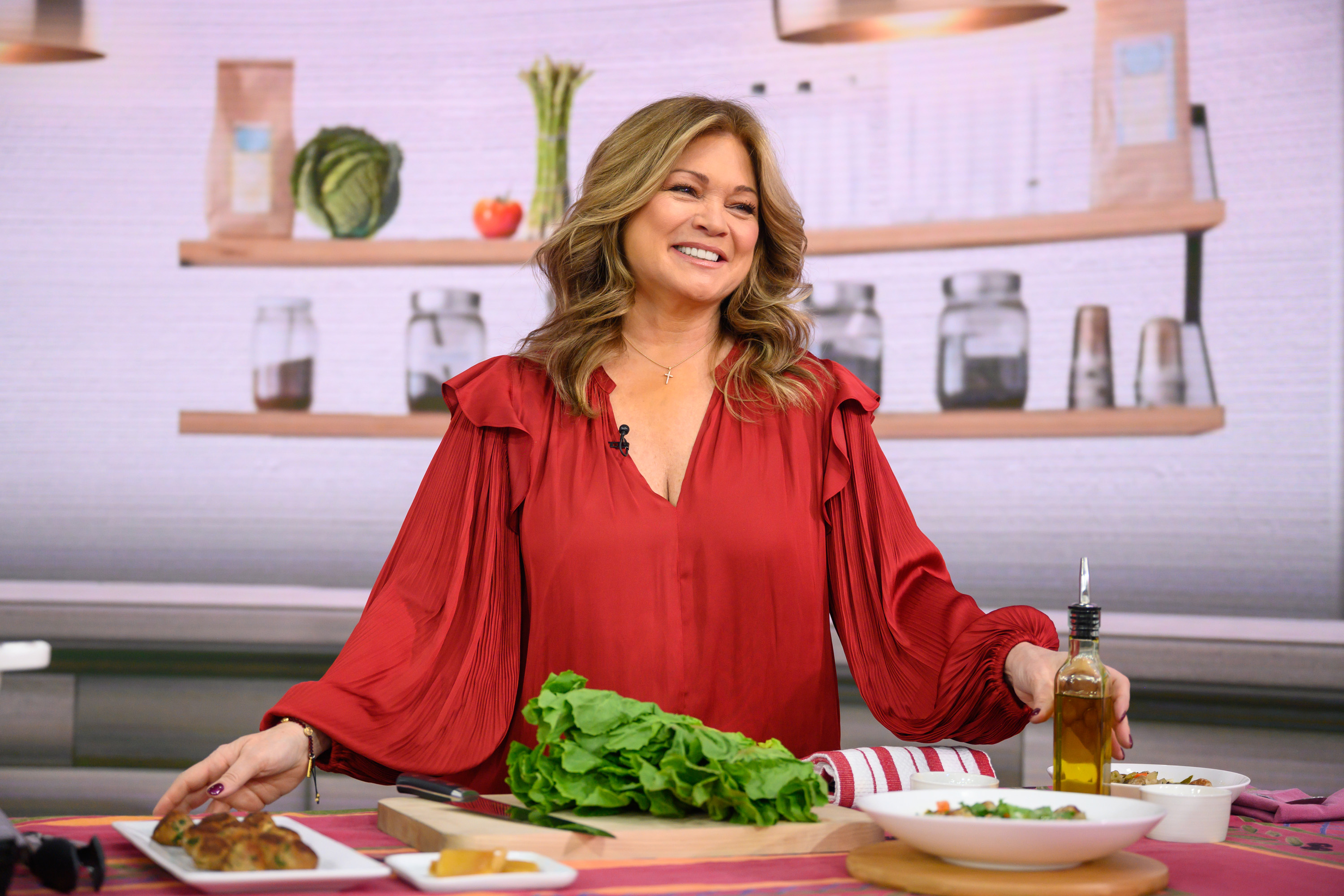 Actor Valerie Bertinelli, who has recently opened up about her weight, wears a long-sleeved red blouse while preparing salad.