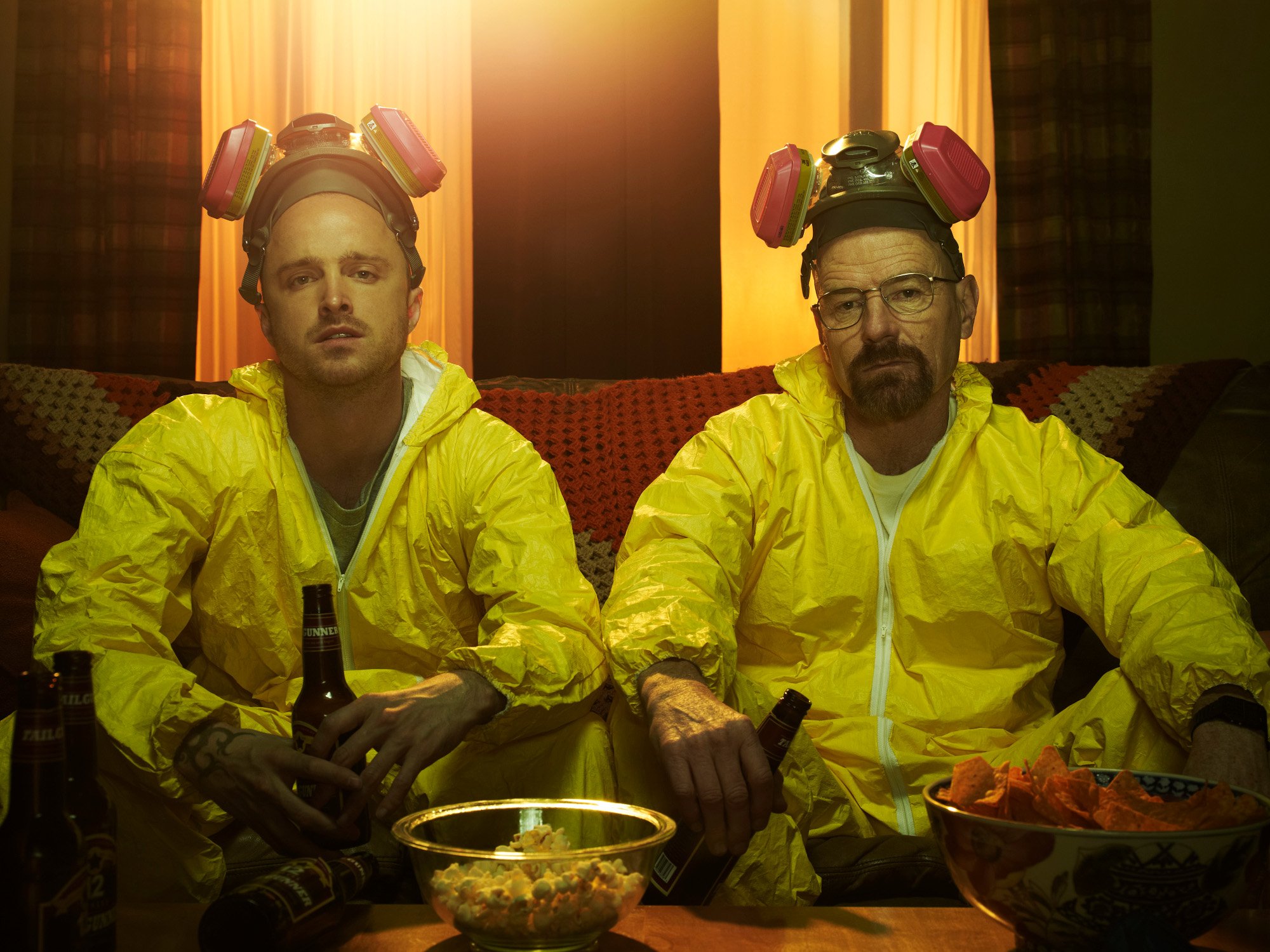 Aaron Paul and Bryan Cranston as Jesse and Walt, both of whom will return in 'Better Call Saul' Season 6 Part 2. They're wearing yellow lab suits and gas masks and sitting on a couch.