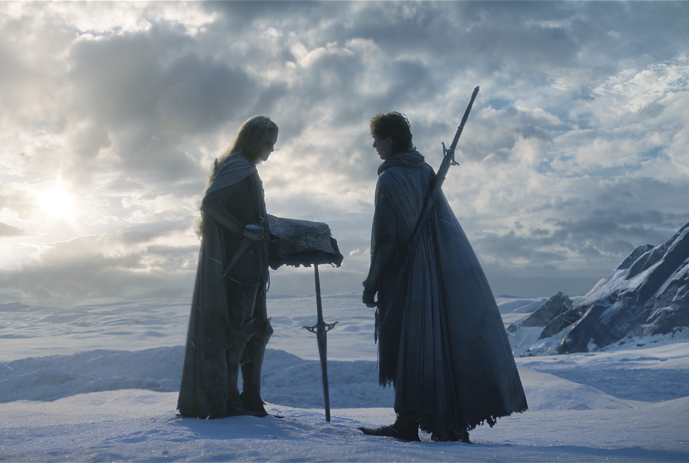 Morfydd Clark and Fabian McCallum in 'The Lord of the Rings: The Rings of Power,' which is set when the Second Age took place. The two are standing amid a snowy landscape. There's a sword sticking out of the ground.