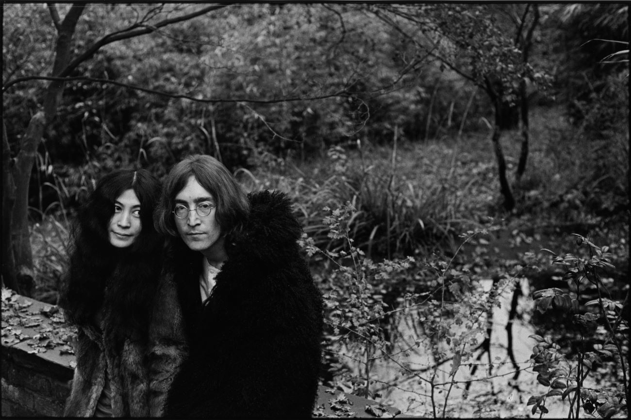 A black and white picture of Yoko Ono and John Lennon outside near a stream.
